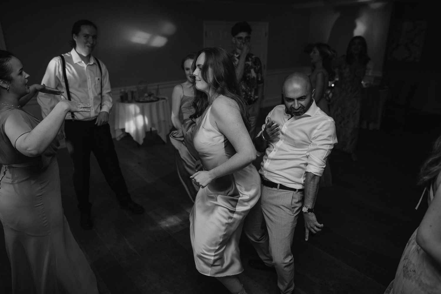 Black and white photo of guests dancing at a dimly lit reception party.