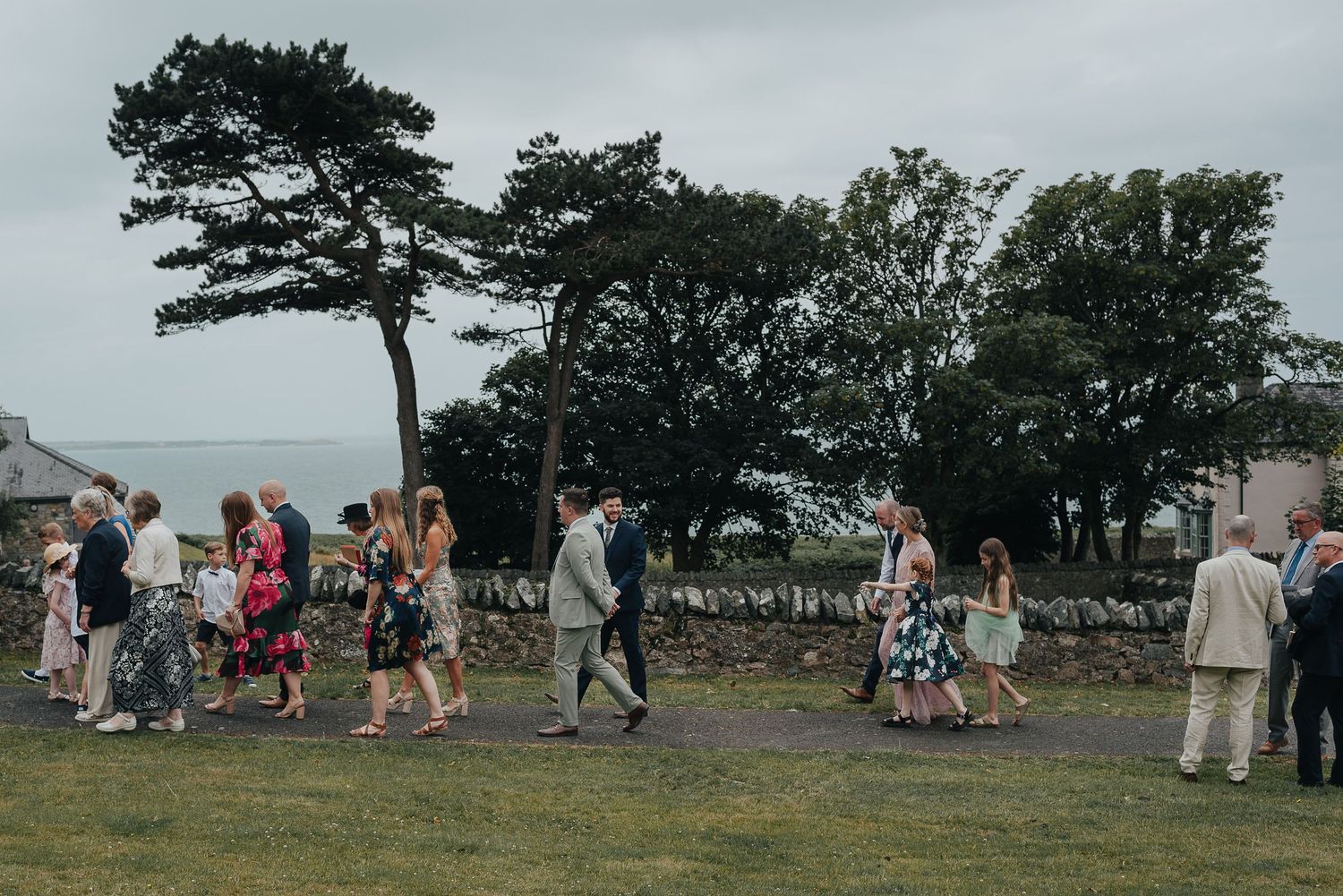 Wedding guests mingling on a lawn overlooking the coastline.