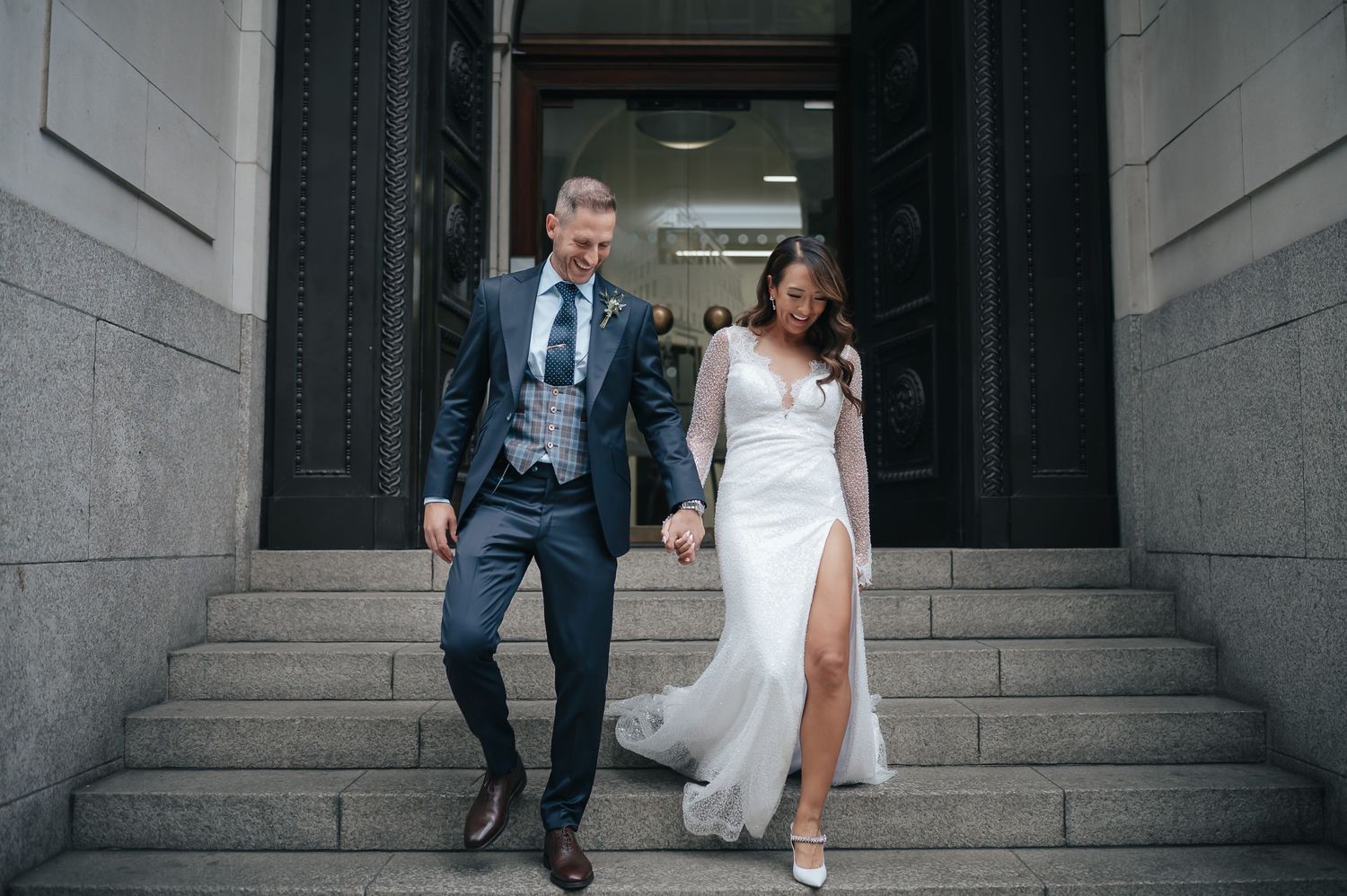 A couple descends stone steps together with joyful expressions during their wedding celebration.