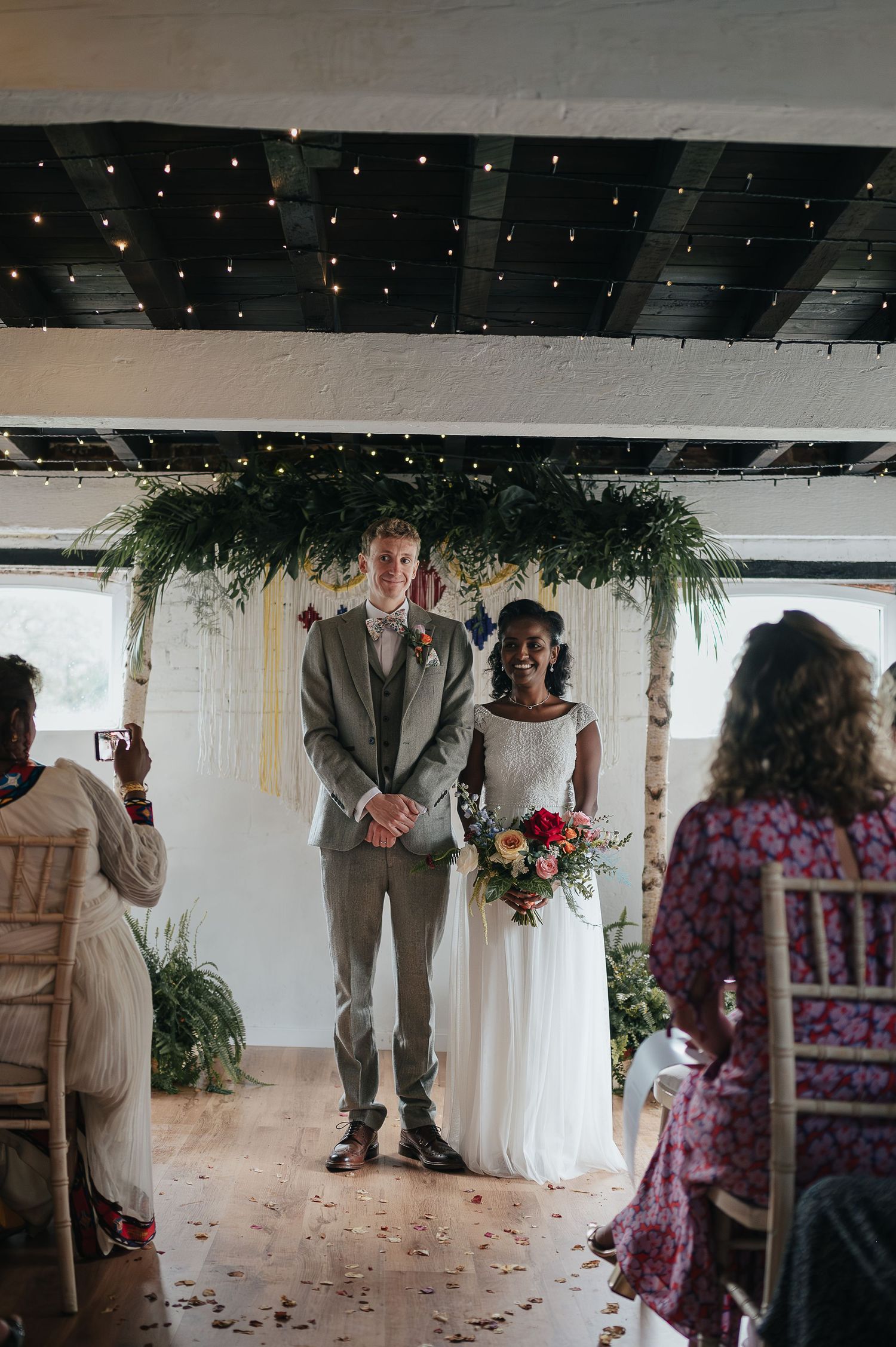 Wedding ceremony under twinkling lights with a beautiful floral arch backdrop.