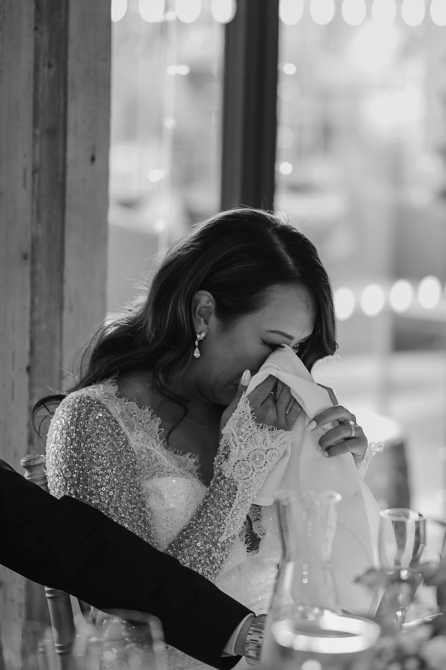 Emotional moment captured in black and white as someone dabs tears with a tissue during a wedding reception.