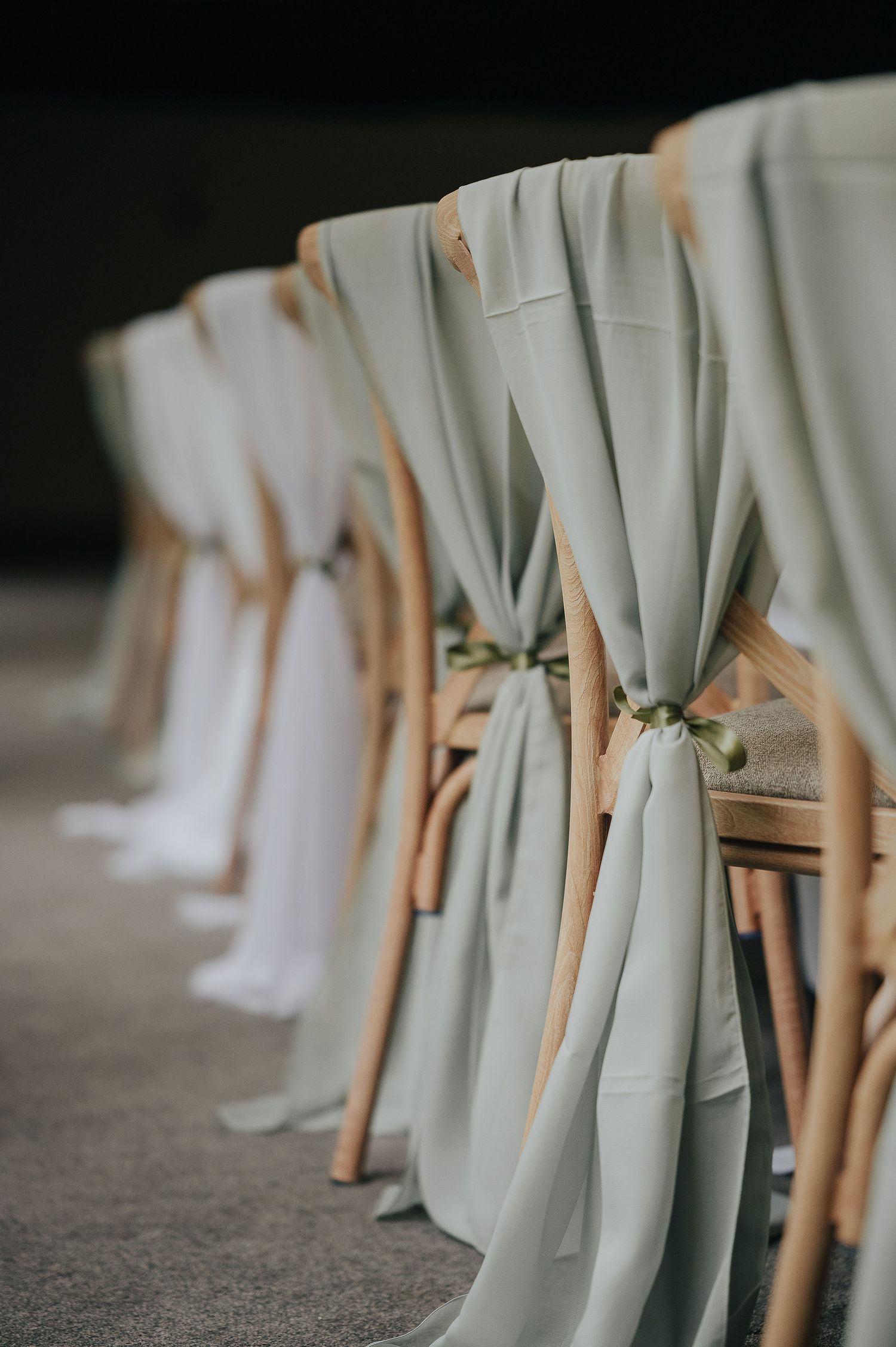Elegant sage green fabric draped on wooden chairs for wedding ceremony decor.