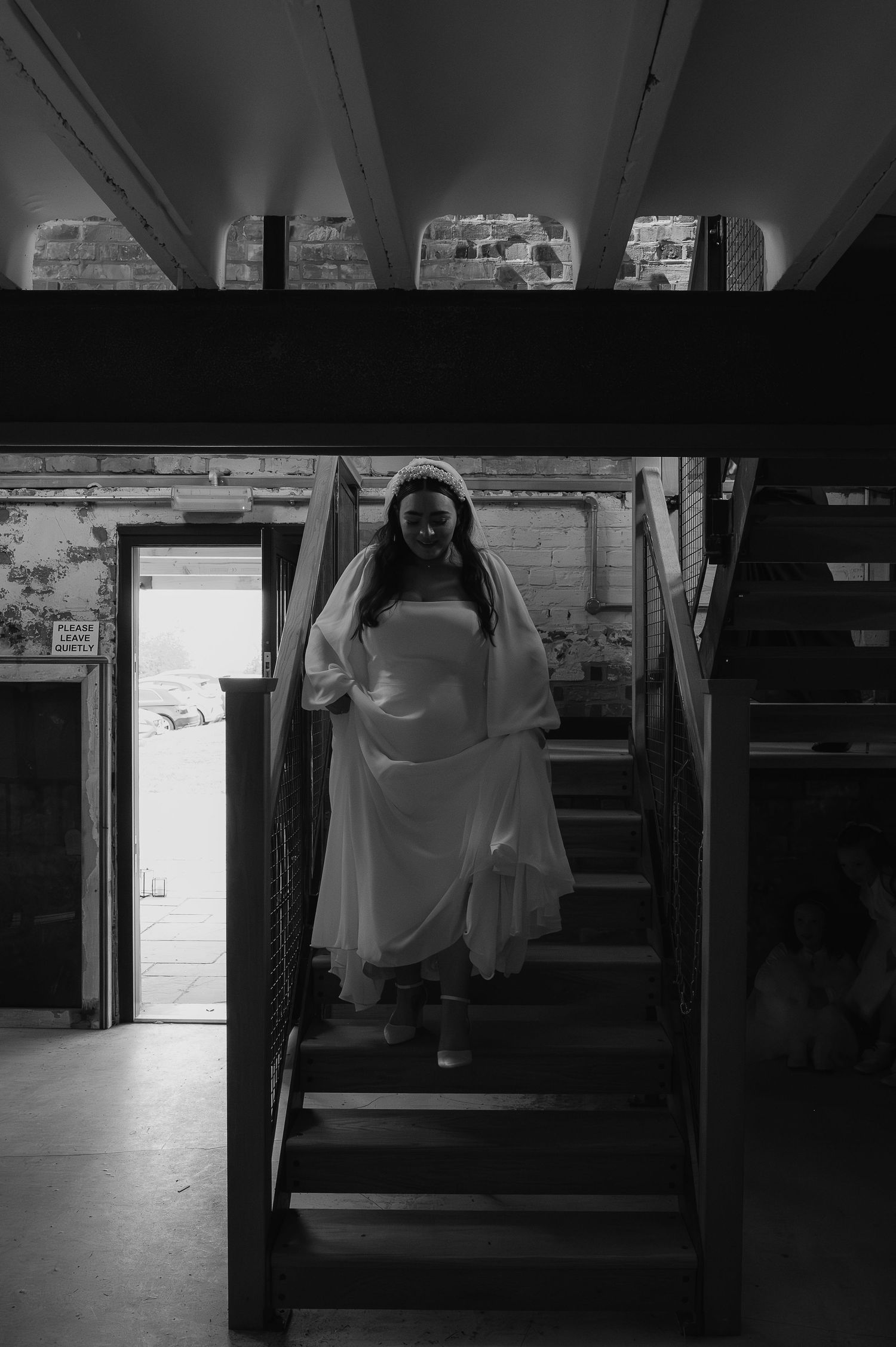 A bride in a flowing white dress poses on dark wooden stairs in a rustic indoor setting.