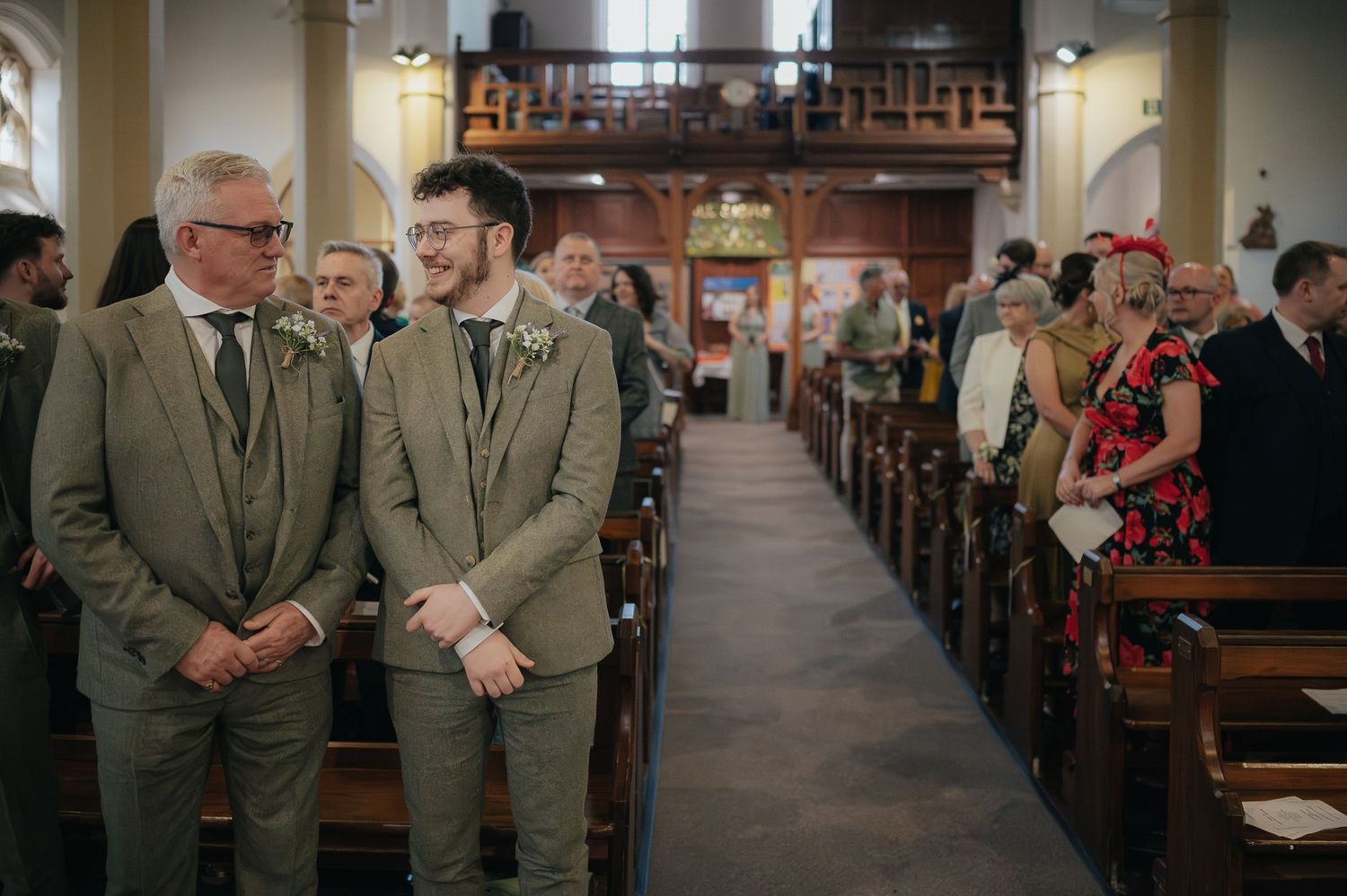 Two people in matching gray suits standing at the front of a church during a ceremony.