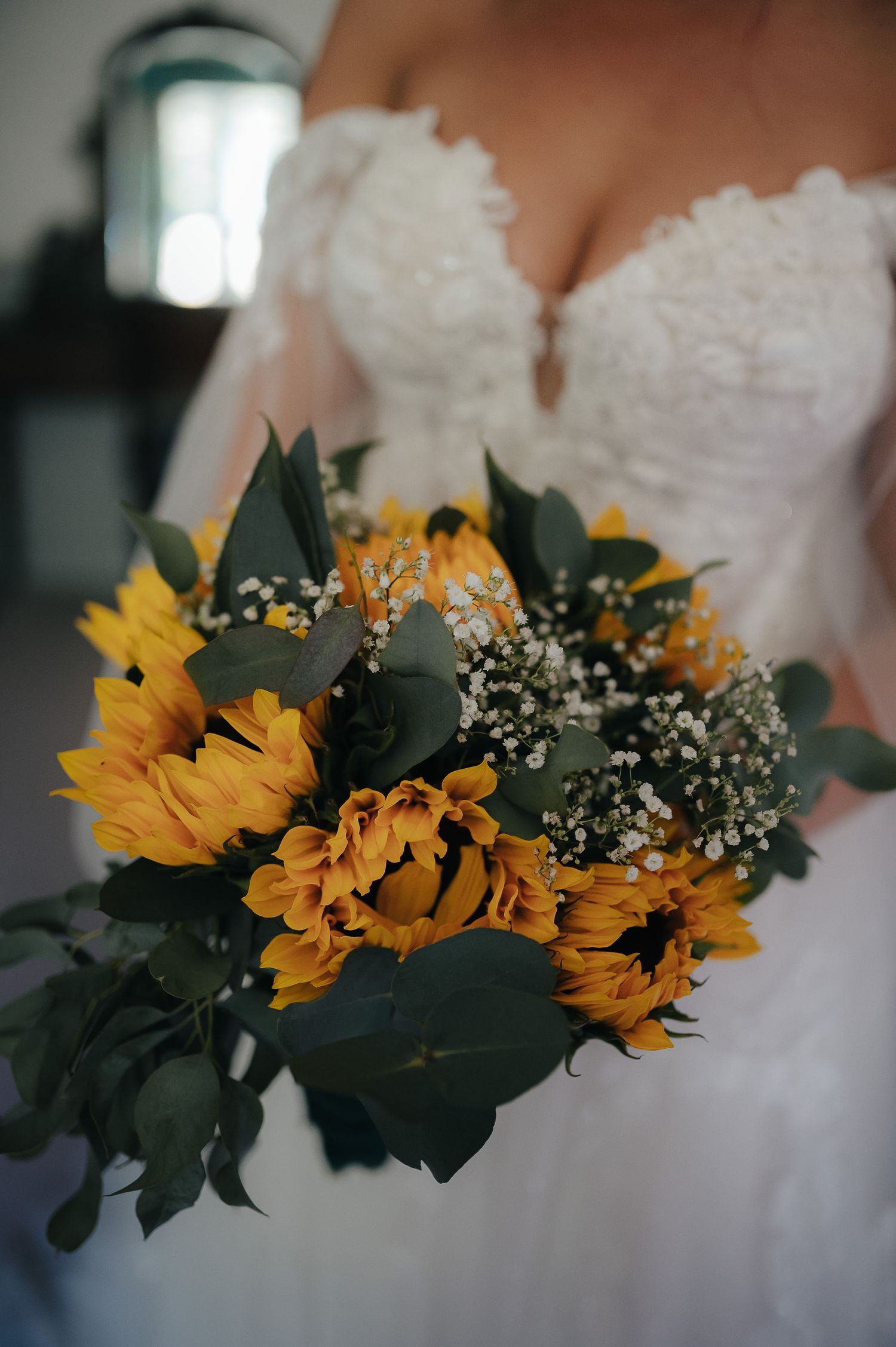 Close-up of bridal bouquet featuring vibrant sunflowers and greenery against white wedding dress.
