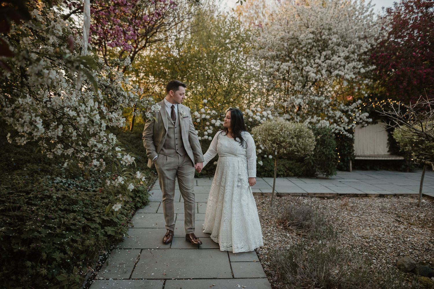 A couple strolls hand in hand through a spring garden with blooming cherry blossoms.