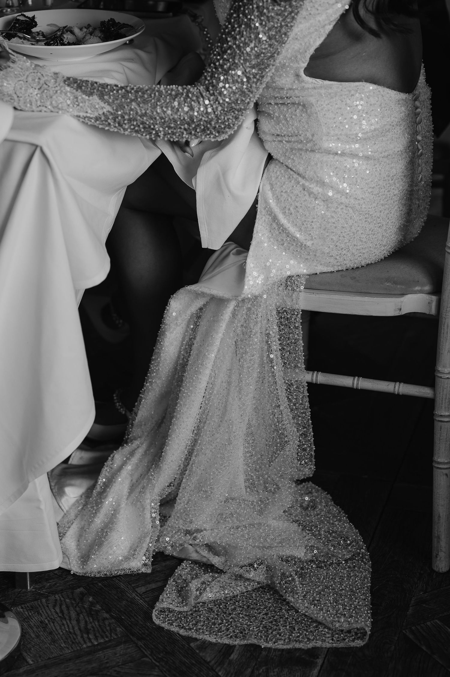 Black and white detail shot of a sparkly wedding dress against formal table settings.