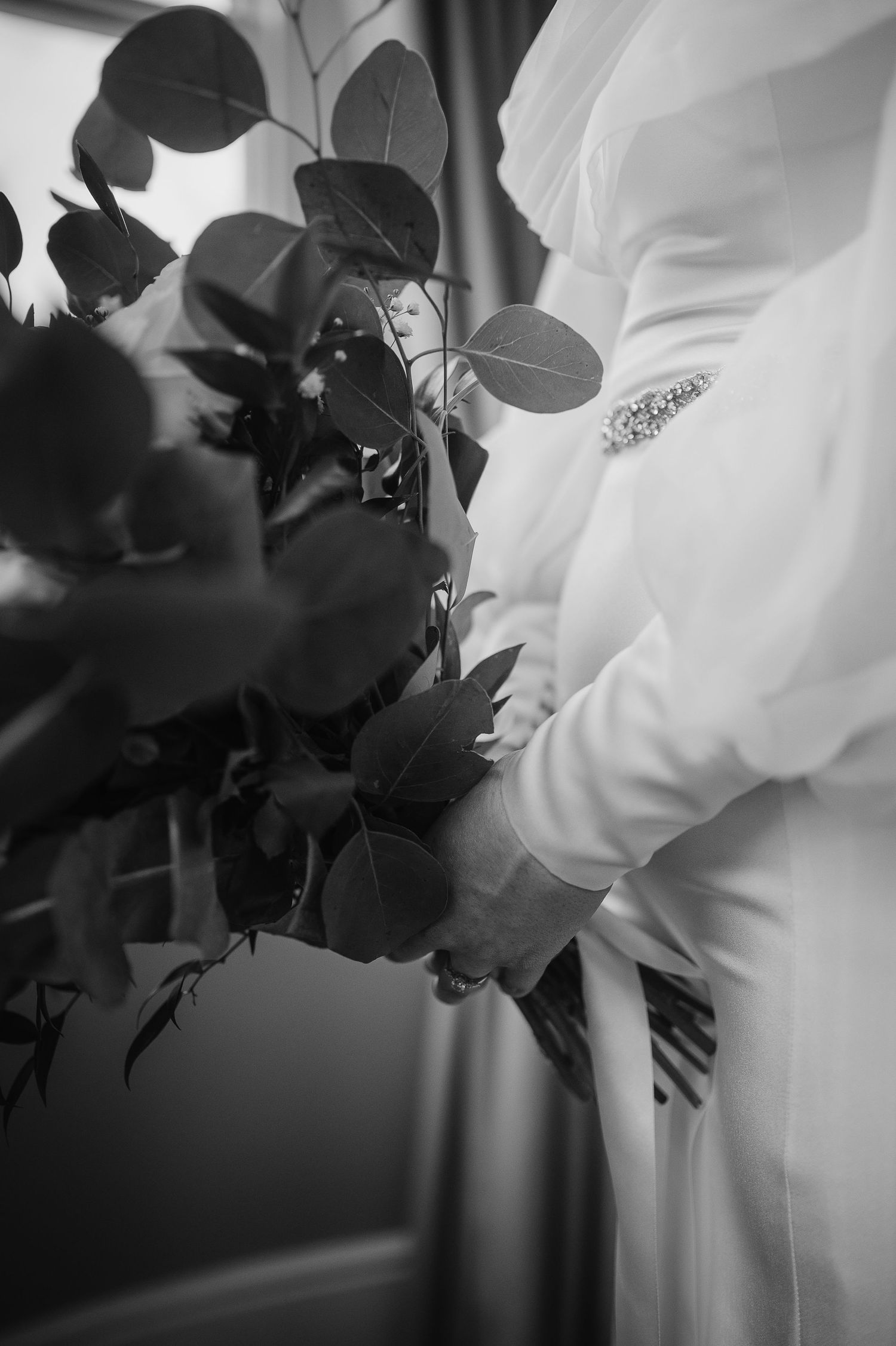 Black and white detail of eucalyptus bouquet against wedding dress fabric.