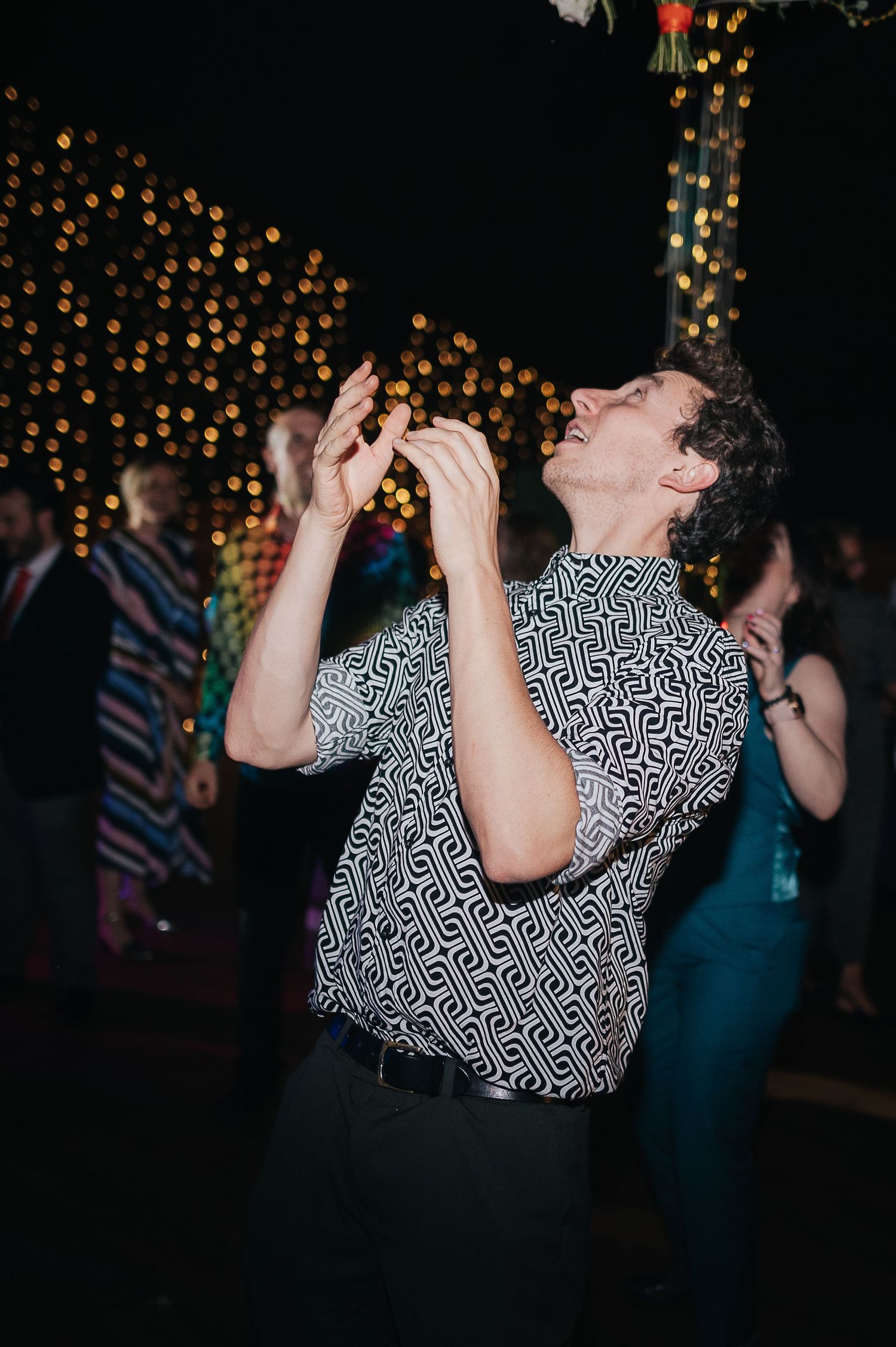 Person in patterned shirt dancing enthusiastically under twinkling lights.