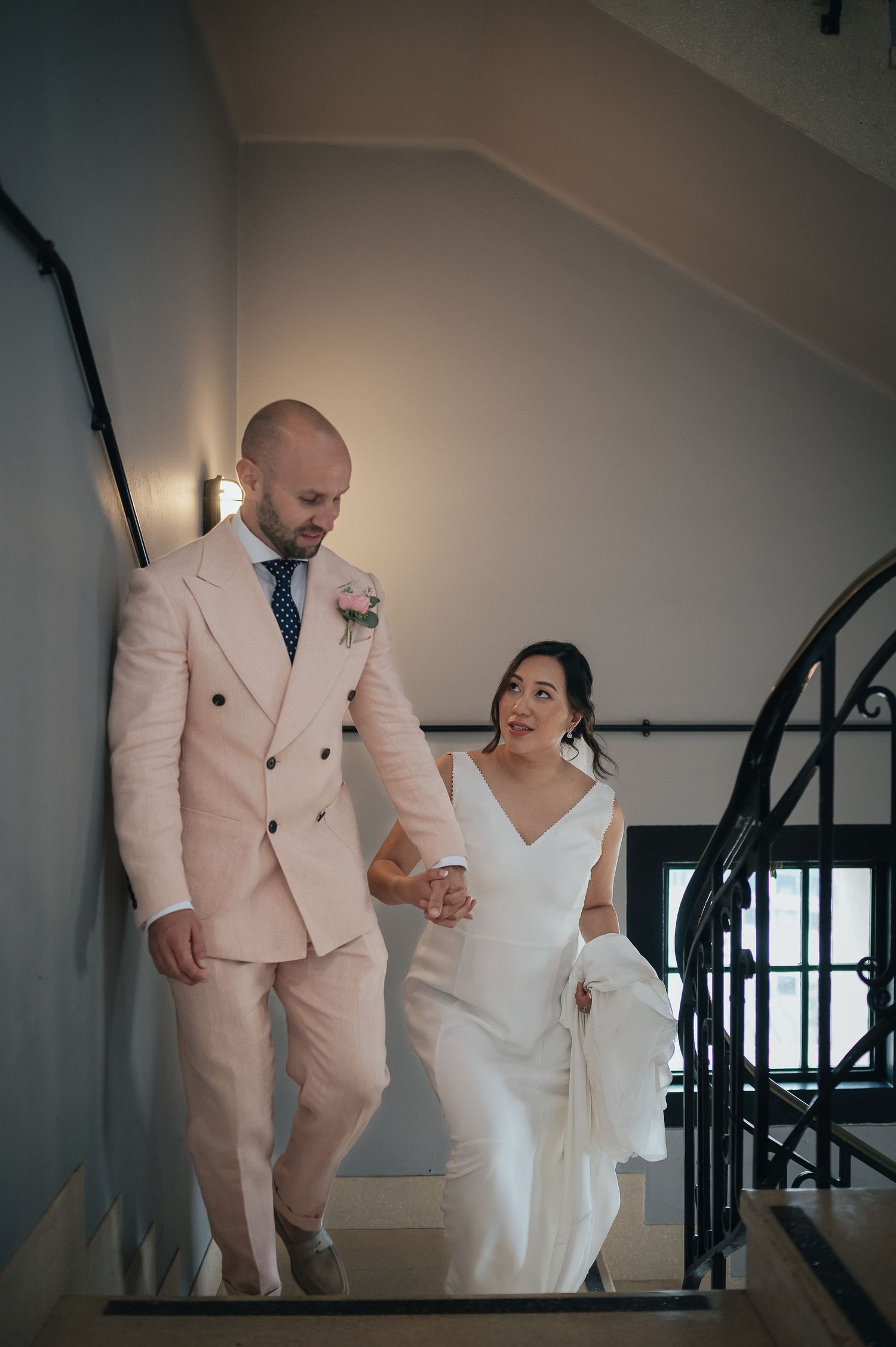 A couple descending a staircase, with the person in a peach suit holding the hand of someone in a white dress.