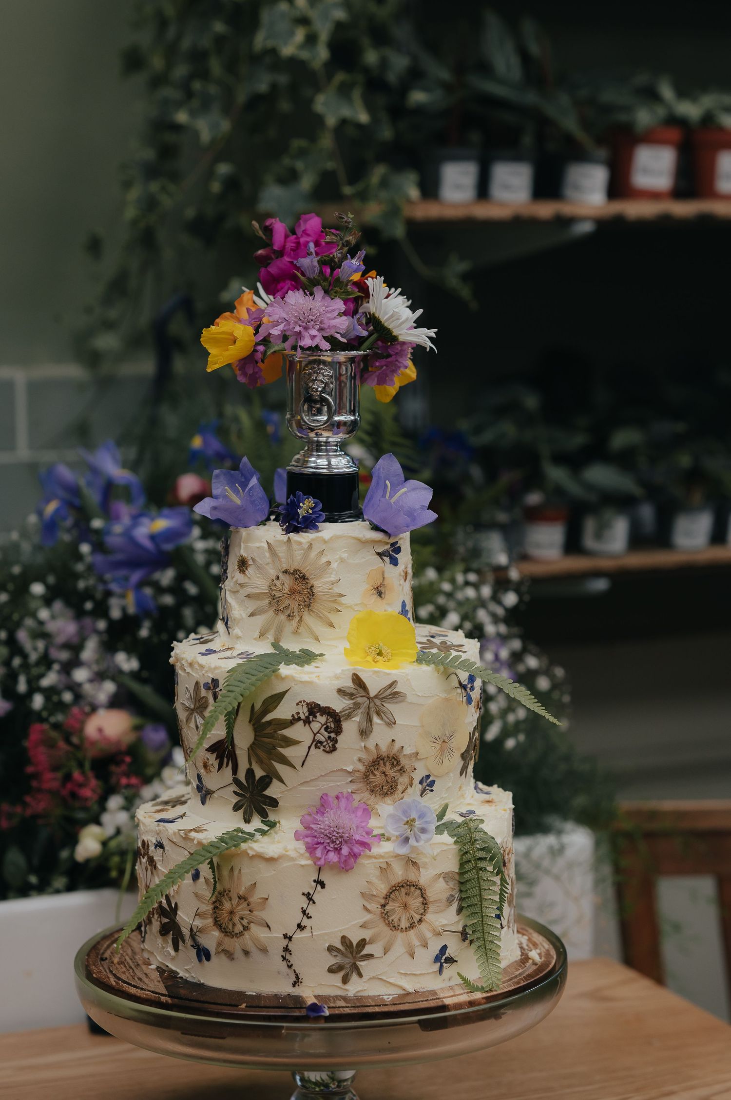 Three-tiered white wedding cake decorated with pressed flowers and fresh blooms.