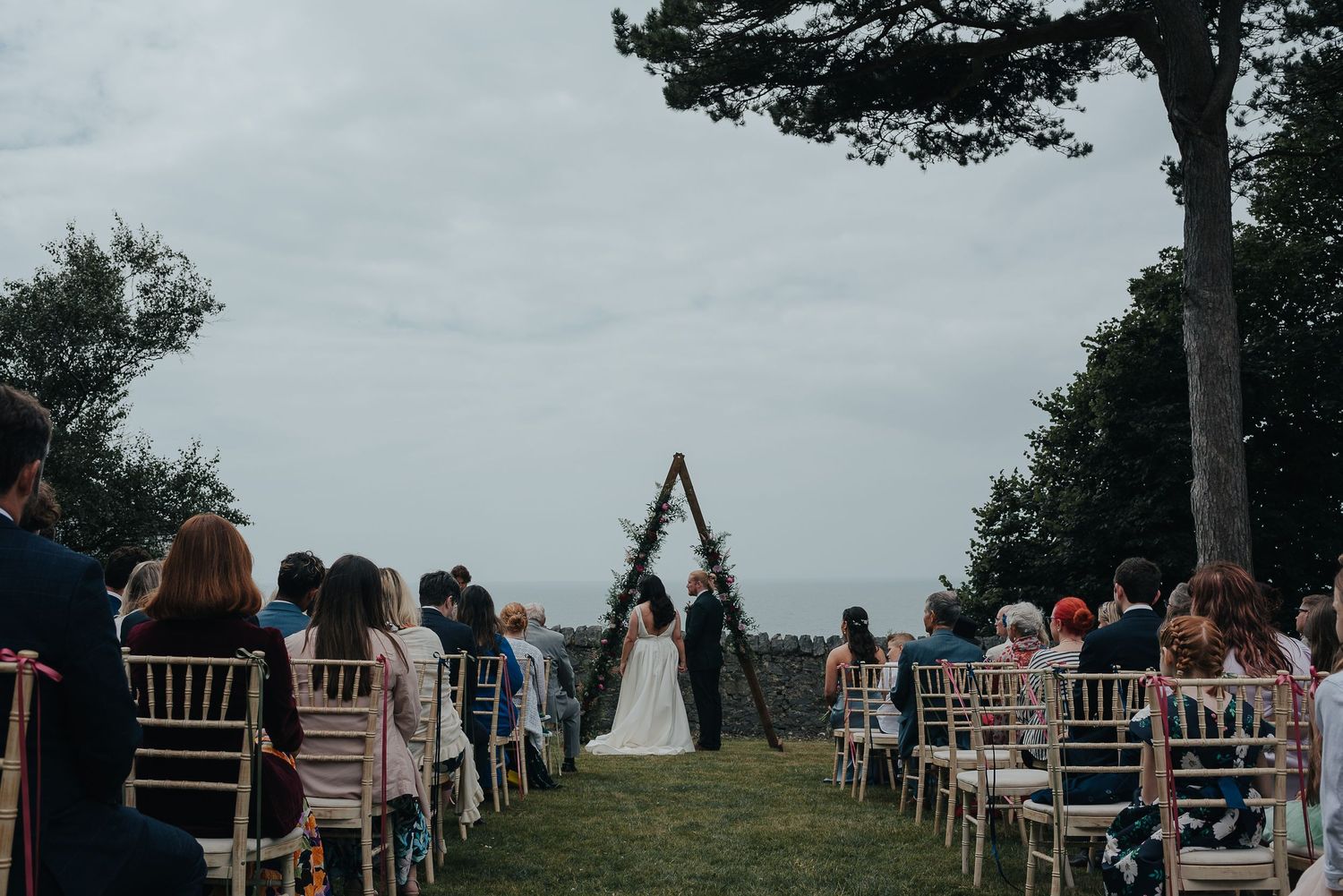 Outdoor wedding ceremony setup with wooden arch and white chairs on a hilltop.