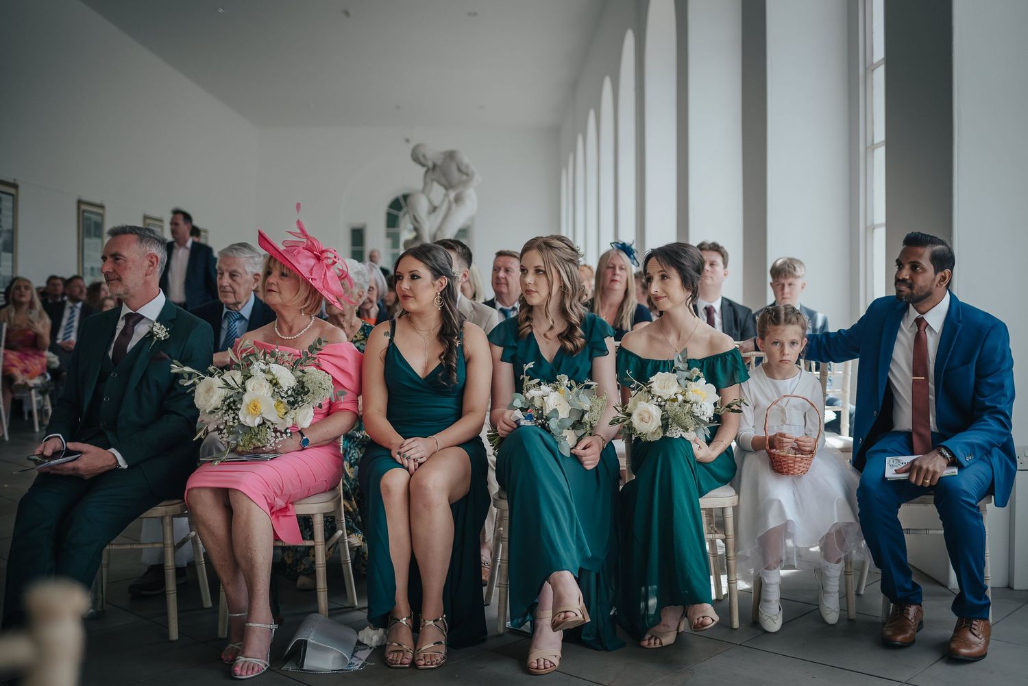 Wedding guests seated in rows at ceremony venue wearing formal attire and bright colors.