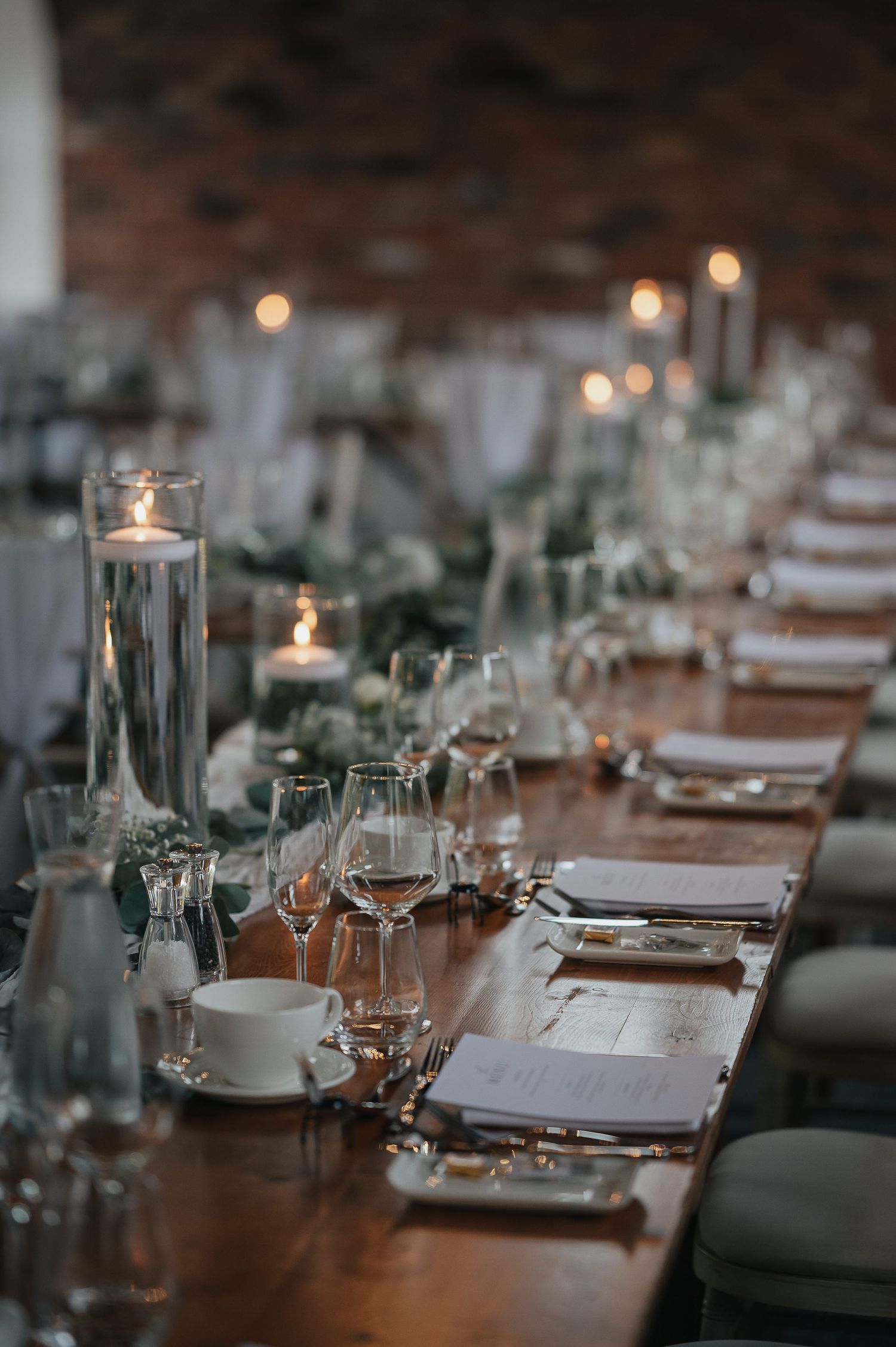 Elegant wedding reception table setting with glassware, candles and greenery decorations.