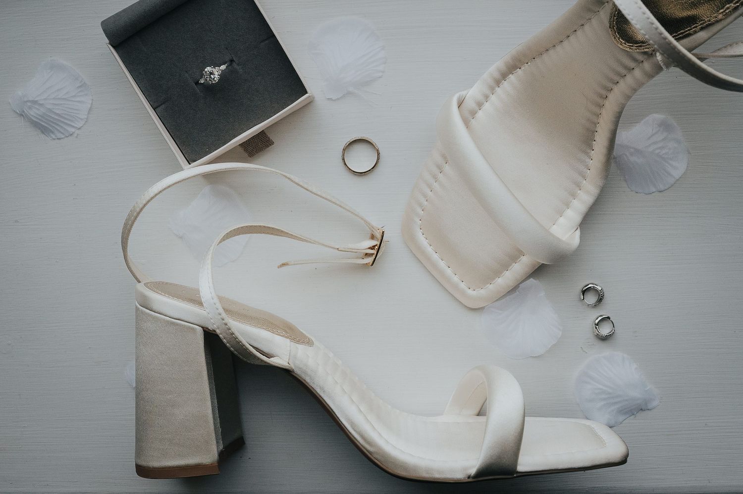 White block heel wedding shoes and rings arranged on a light surface.