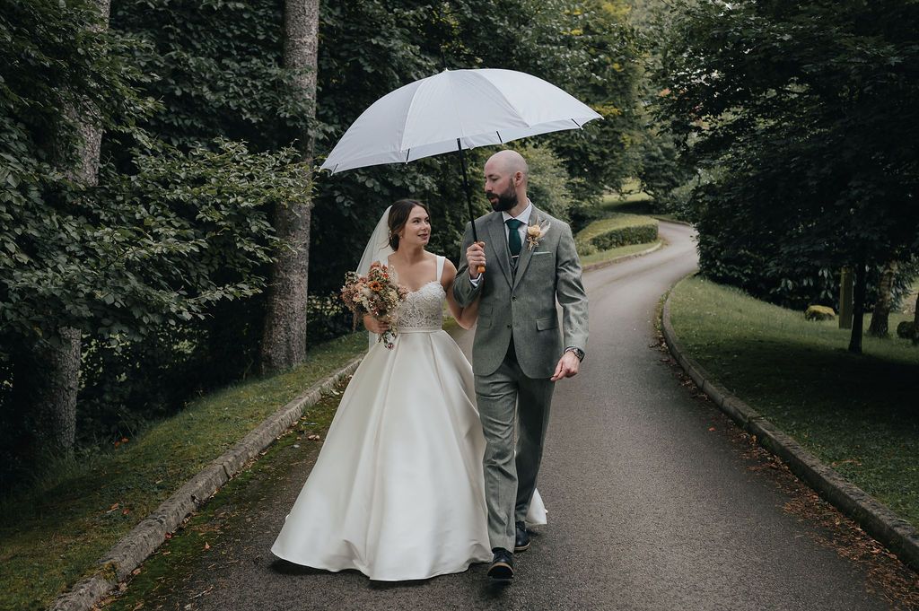 Newlyweds walking along a curved path under a white umbrella.