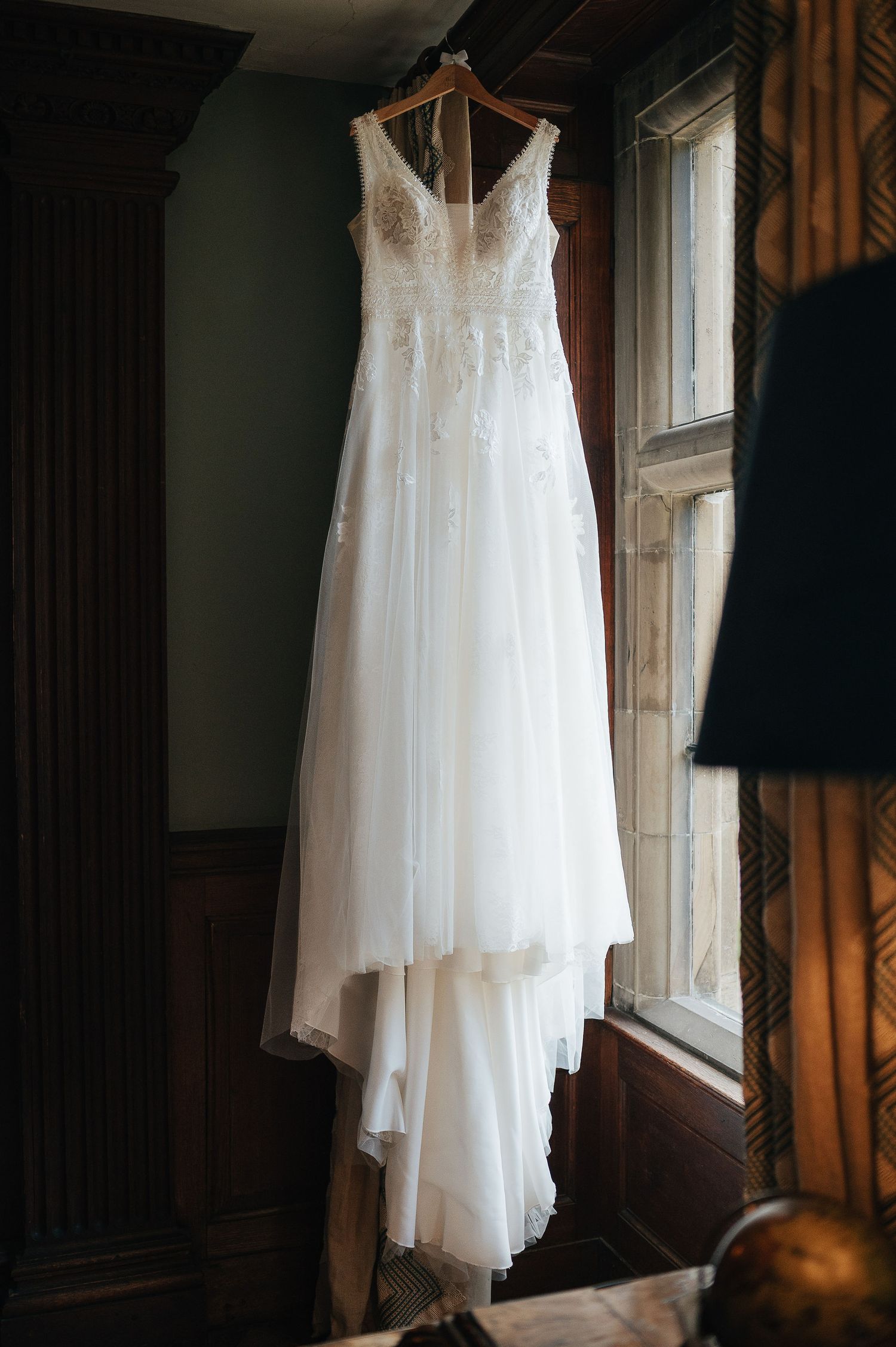 Elegant white wedding dress with lace details hanging by window in preparation for the big day.