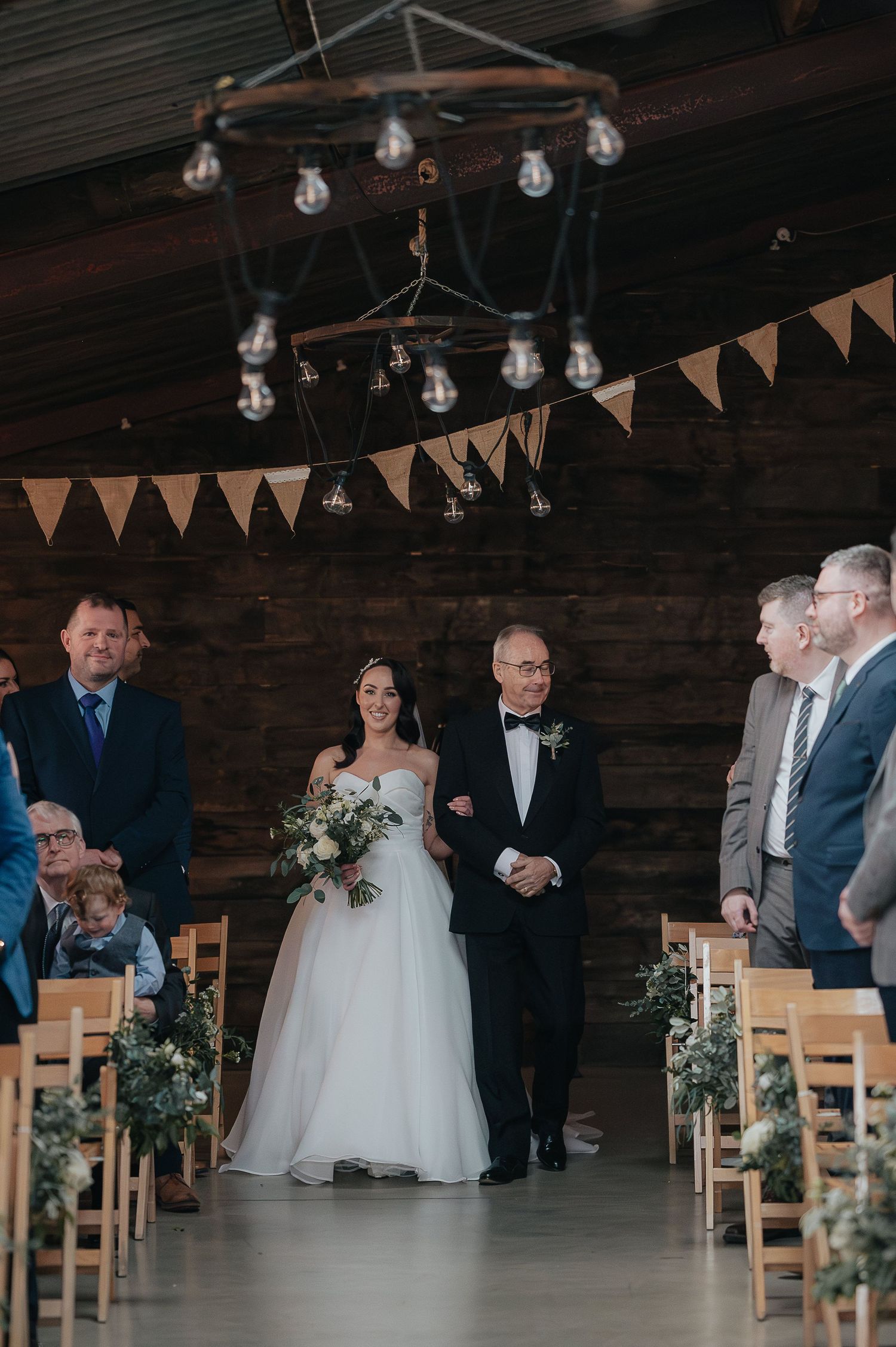 Wedding ceremony setup with string lights and bunting in rustic wooden venue.
