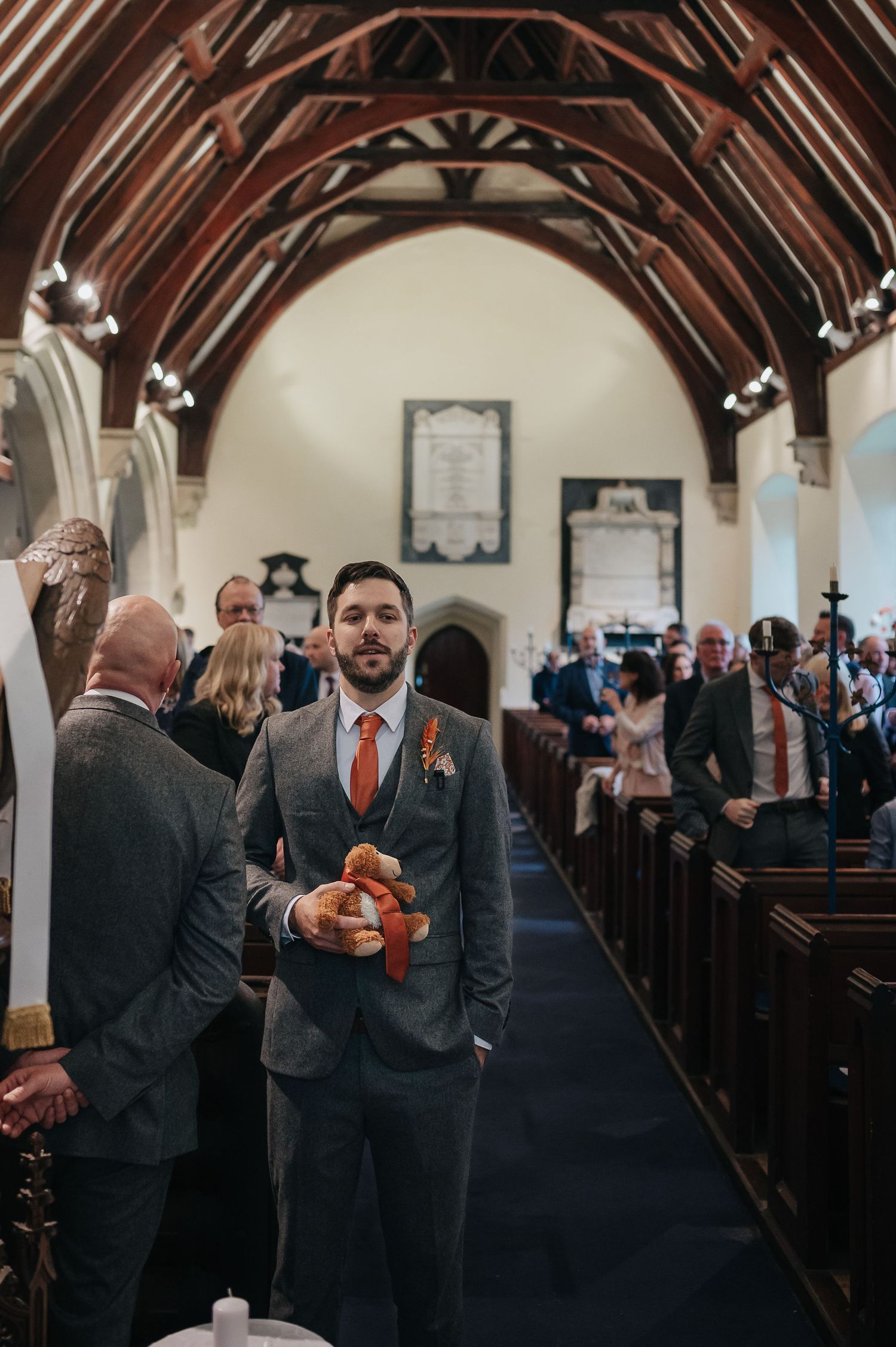 Inside a church with wooden arched ceiling, wedding guests gather in the center aisle.