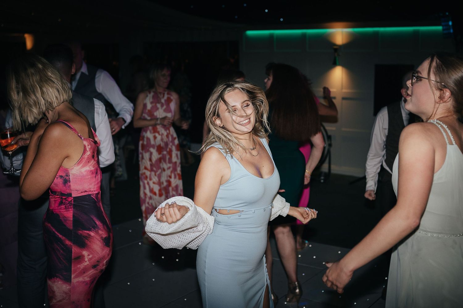 Wedding guests enjoying themselves on a dimly lit dance floor during the reception celebration.