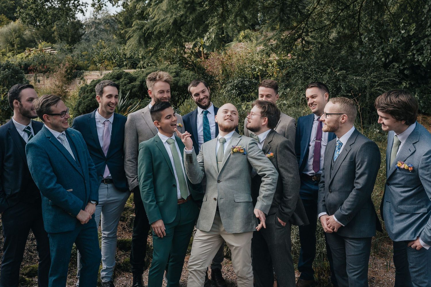 A group wearing suits gather outdoors for a formal wedding photo.