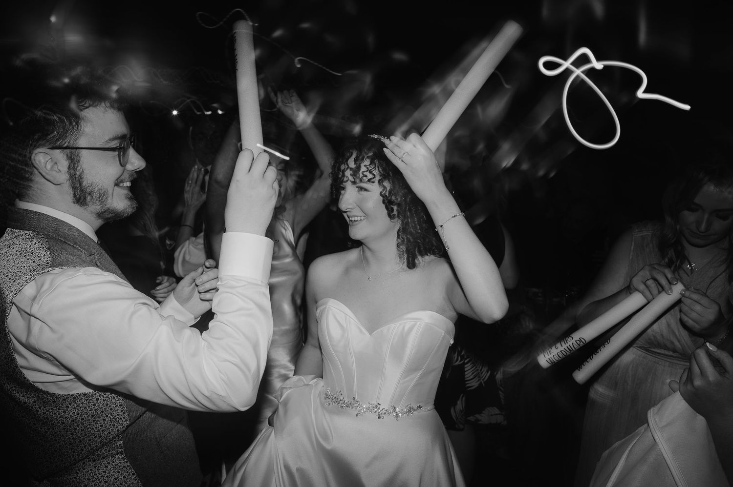 Wedding celebration with guests dancing and raising their arms on a dark dance floor.