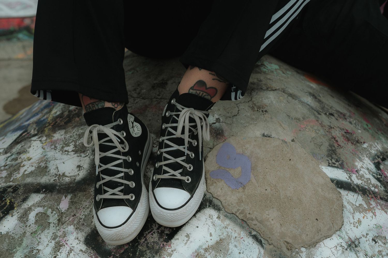 A sequence of black and white Converse sneakers shown from different angles on a concrete surface.