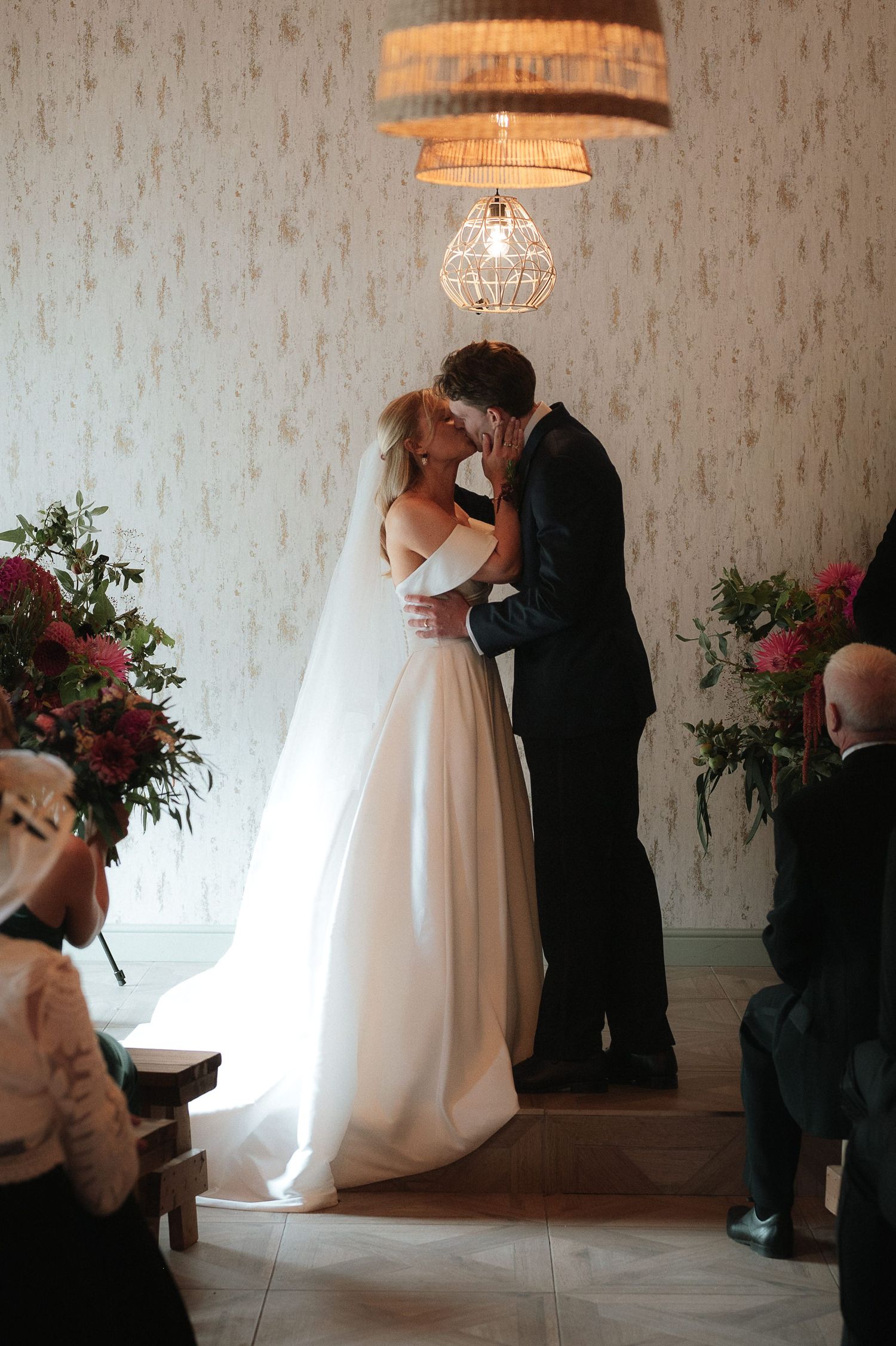 Intimate wedding ceremony under a geometric chandelier with red floral arrangements.