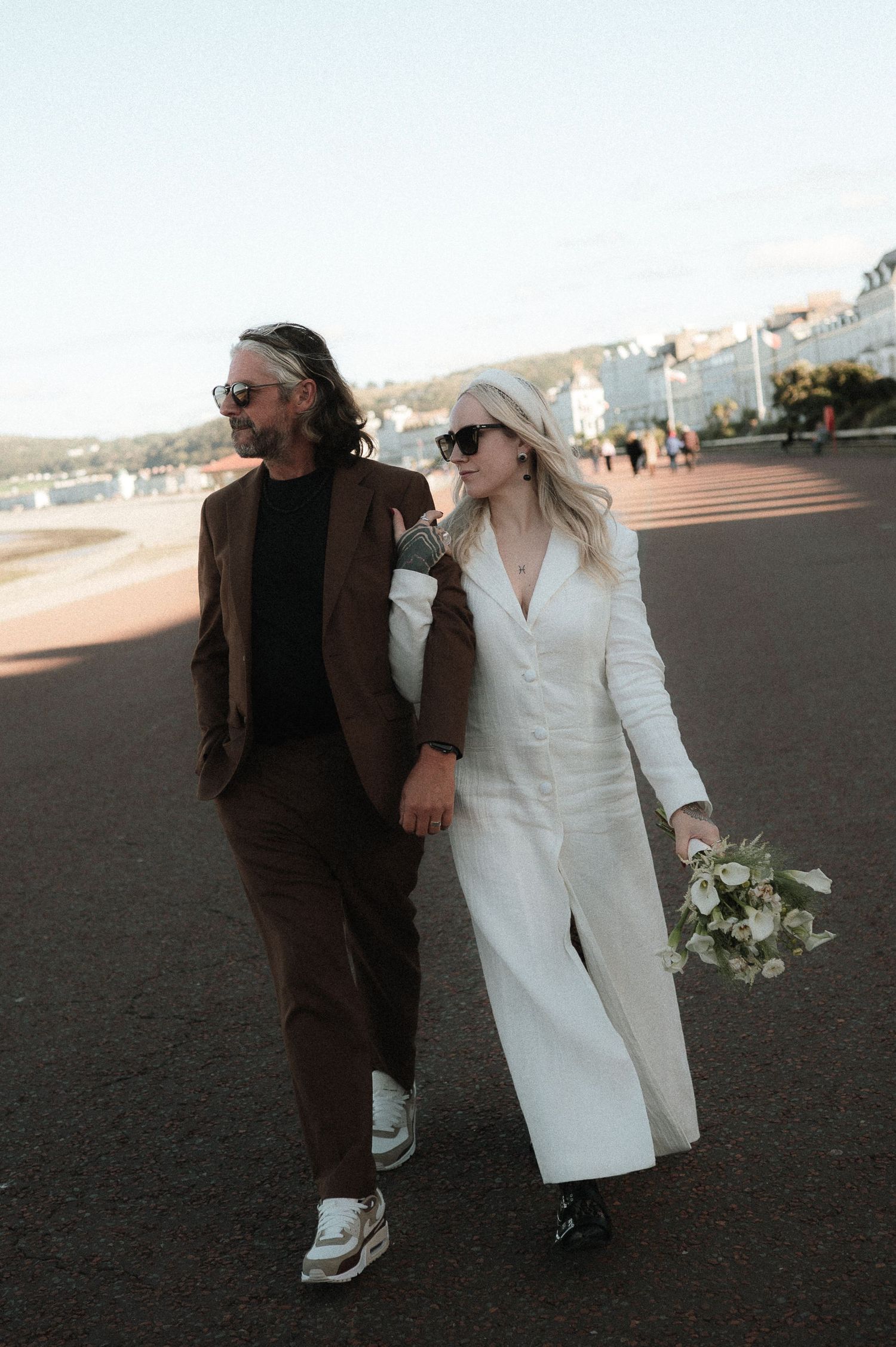 Couple walking together on pavement at sunset wearing contrasting brown and white outfits.