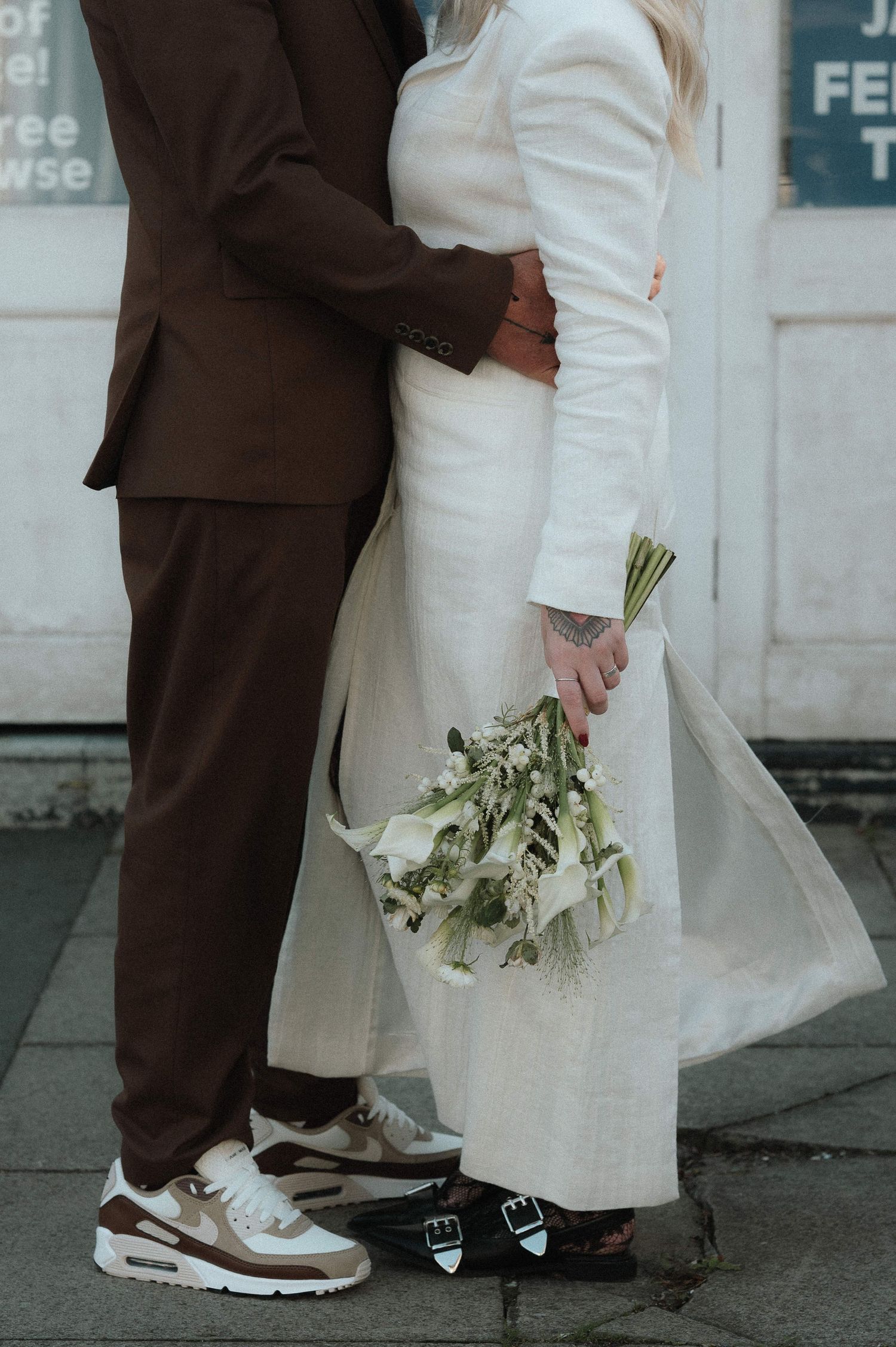 Close-up of contrasting brown and white outfits with sneakers and floral bouquet.