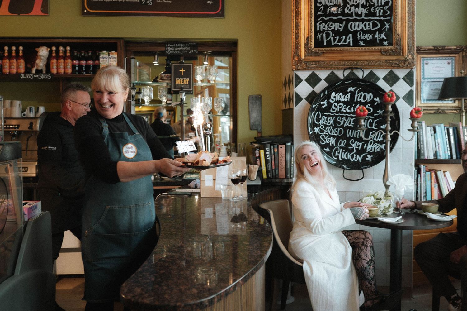 People gathered inside a cozy pub or restaurant with chalkboard menus on the wall.