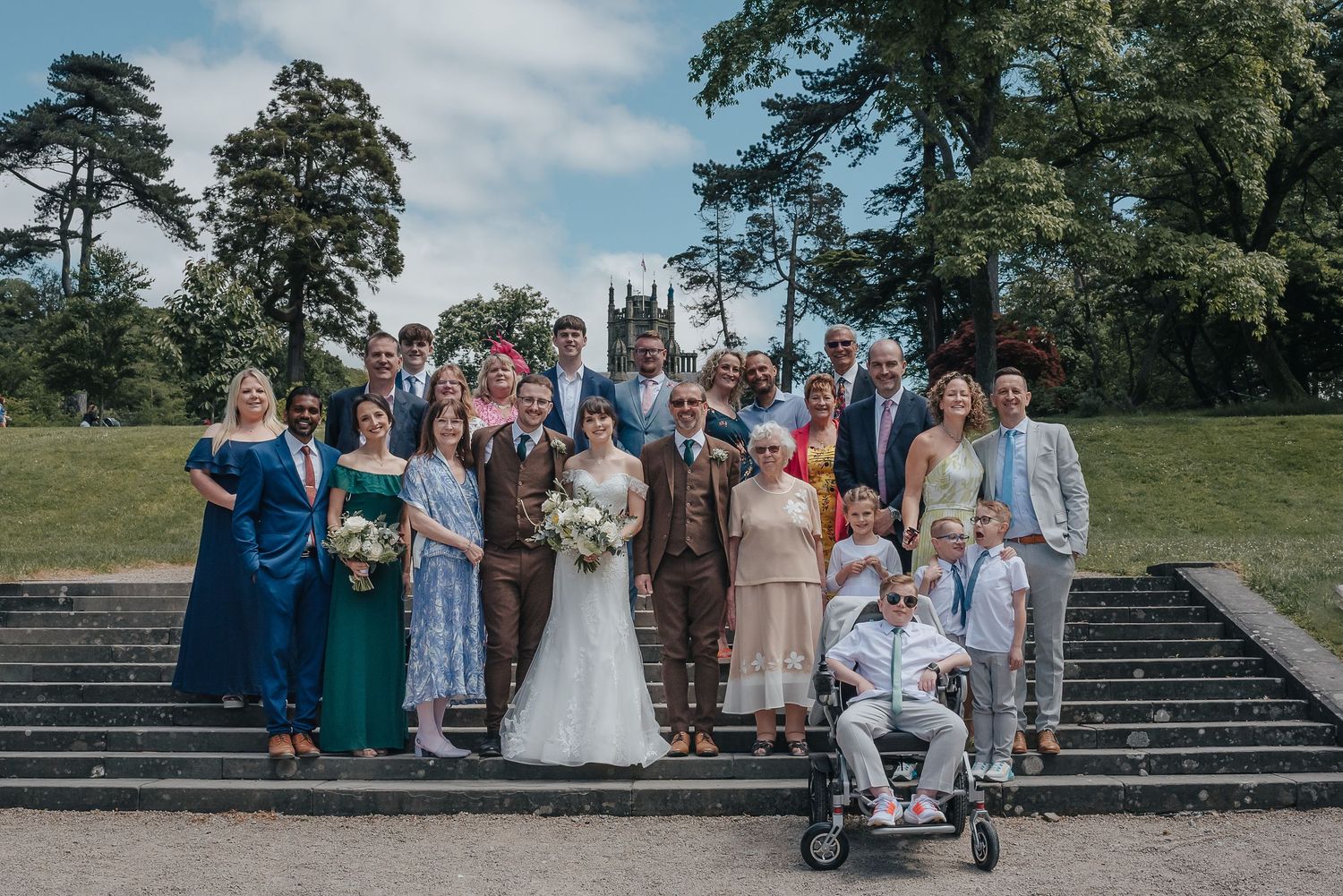 Wedding party gathered on stone steps outdoors with trees in the background.