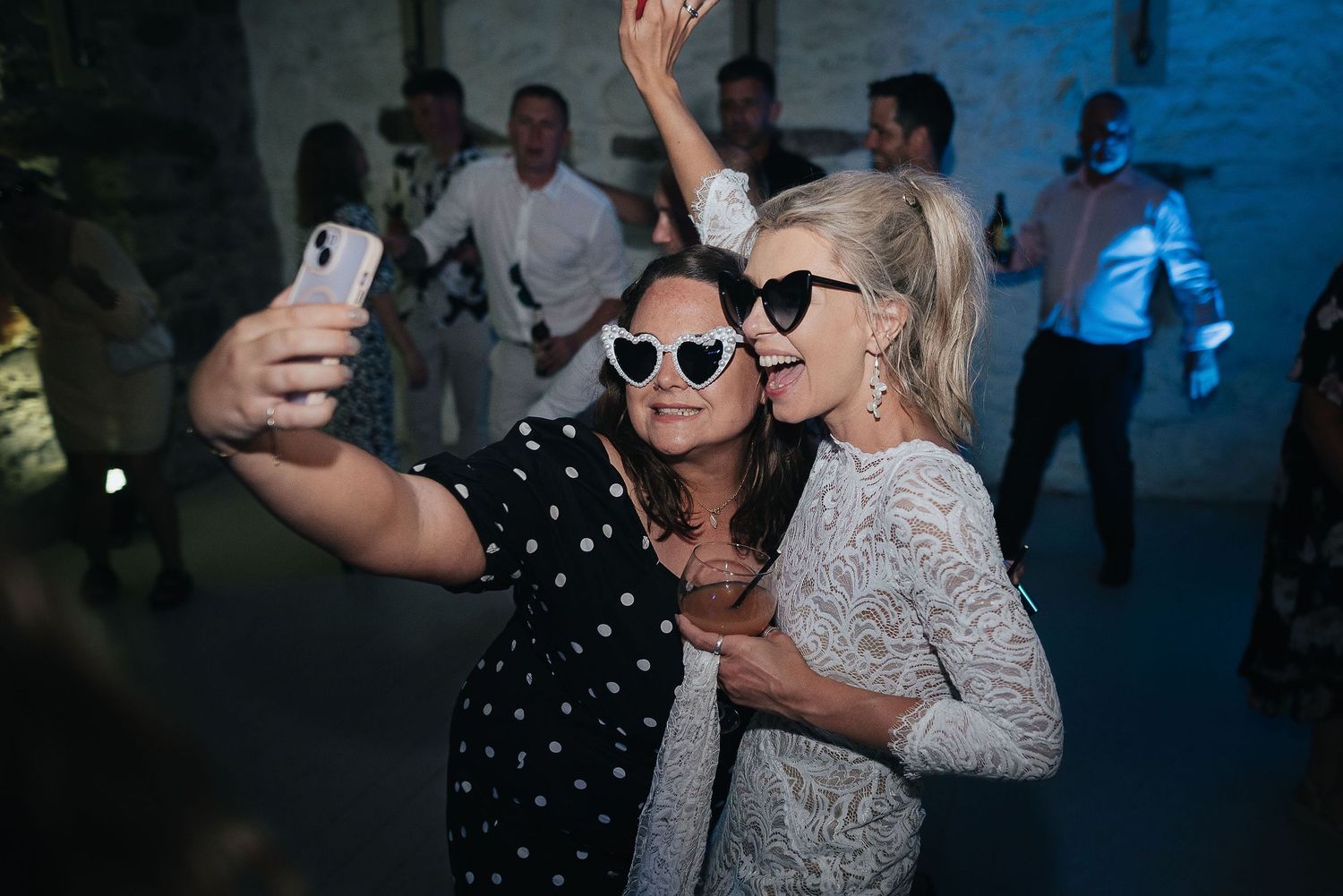 Two guests taking a selfie together during a wedding reception with blue lighting.