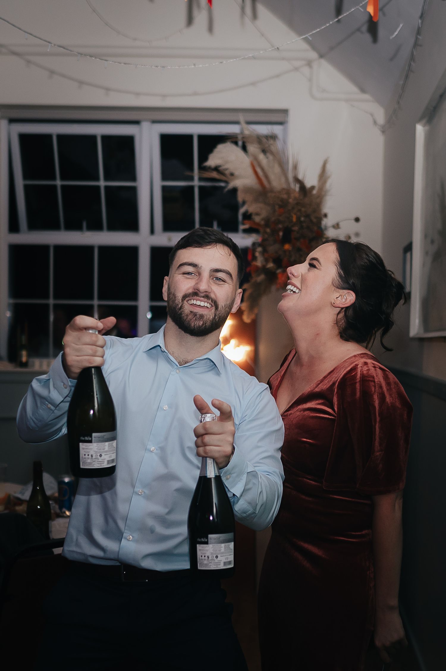 Two guests share a joyful moment with champagne bottles at a celebration.