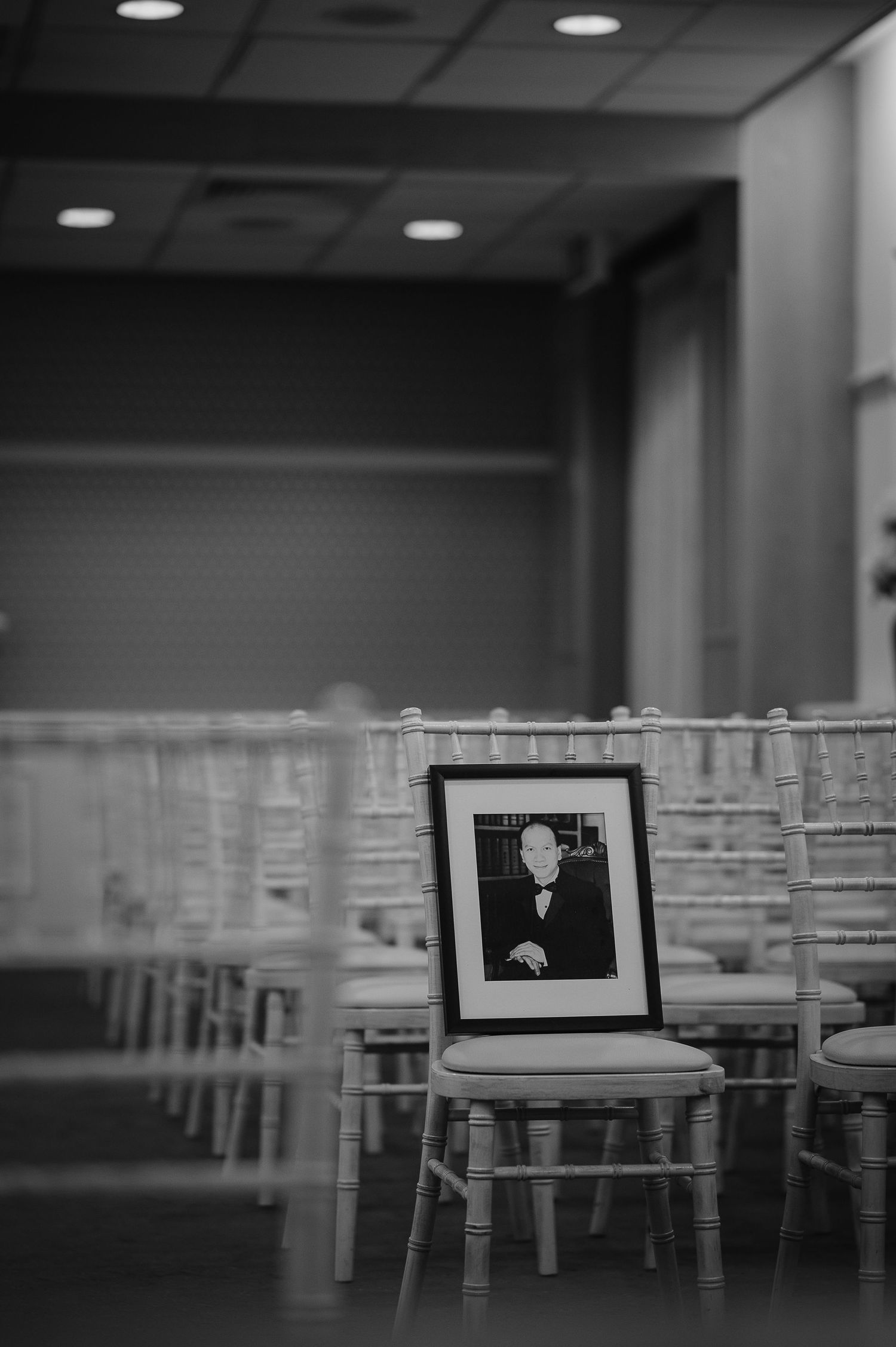 Black and white photo of framed portrait placed on empty chair in ceremony setting.
