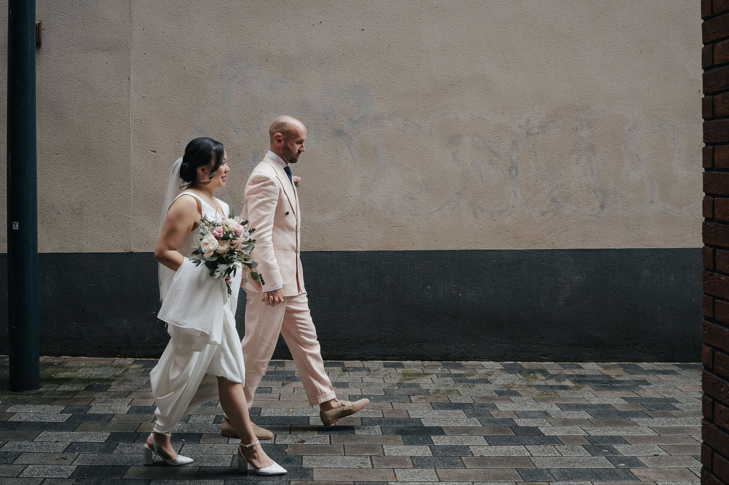 Wedding couple walking together on cobblestone street in elegant attire.