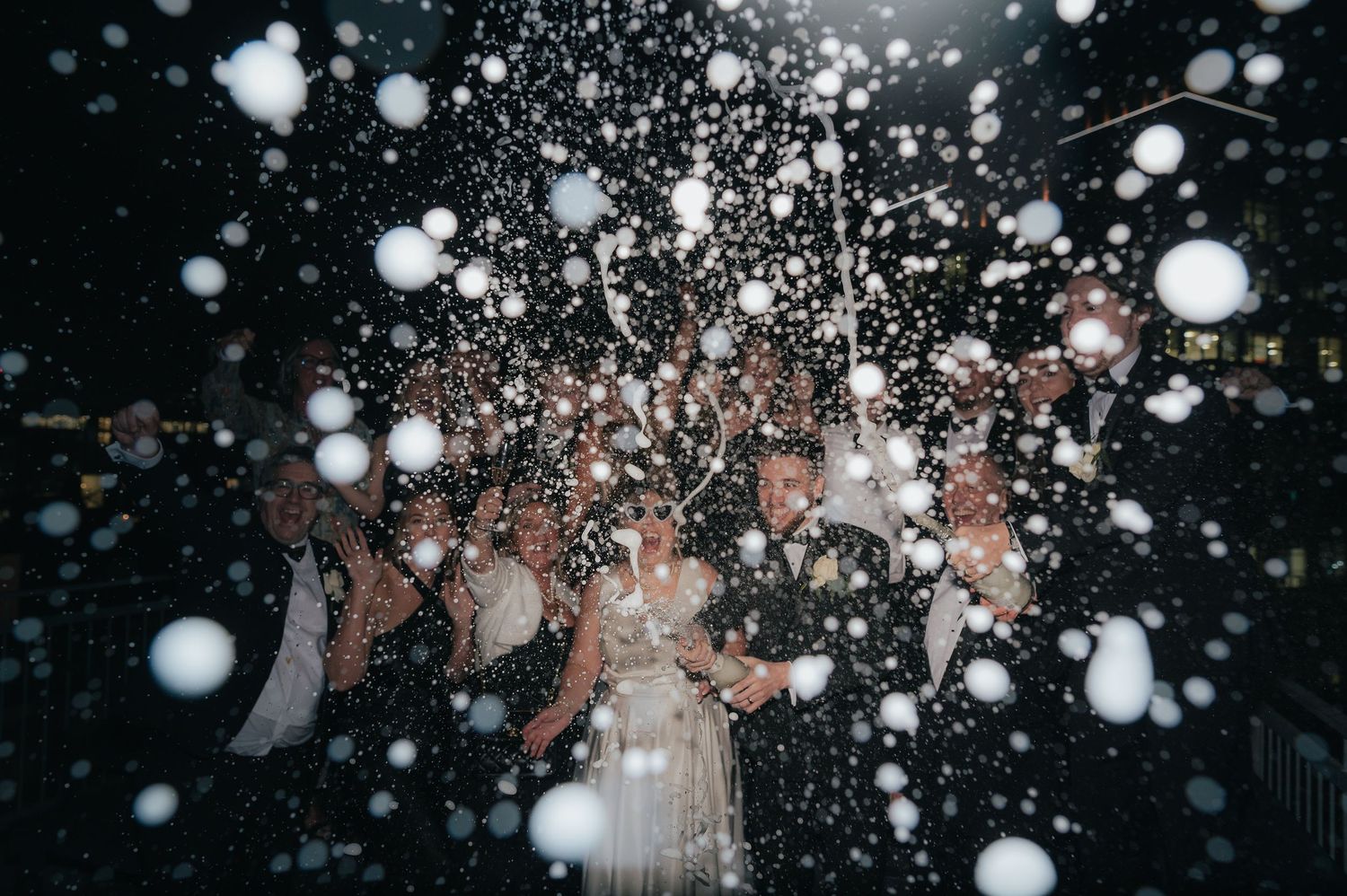 White snowflakes fall against a dark night sky creating a magical winter scene with glowing bokeh light effects.