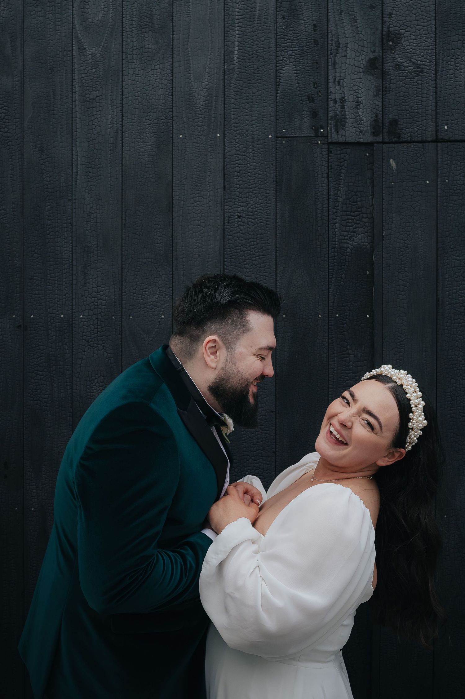 Candid wedding portrait against dark wooden wall showing genuine laughter.