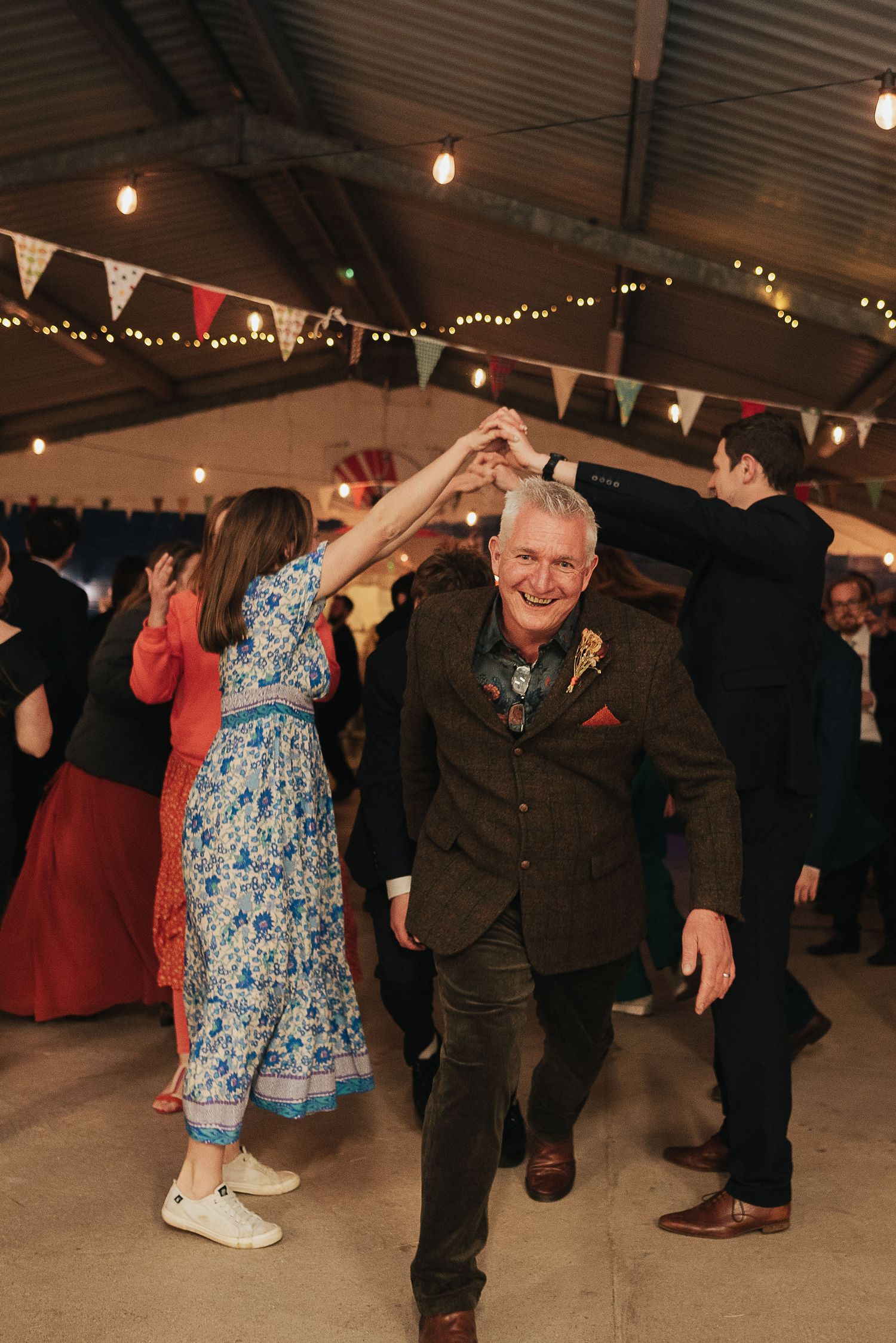 Wedding guests dancing under bunting and fairy lights at an indoor celebration.
