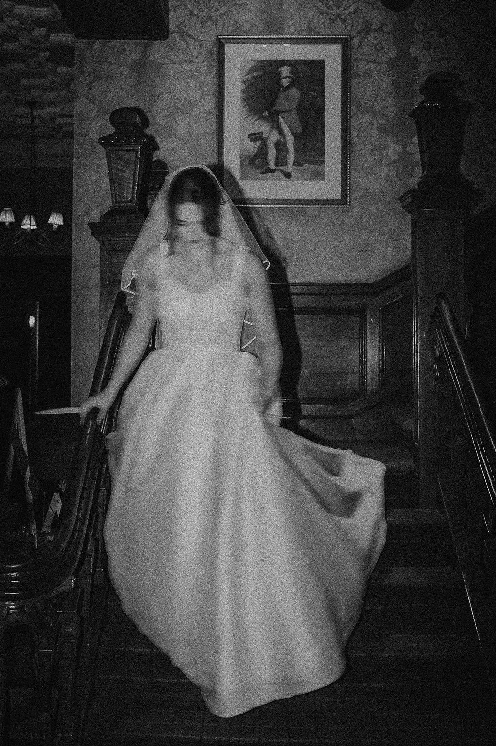 Artistic black and white photo of a flowing white gown on a dark staircase with vintage decor.