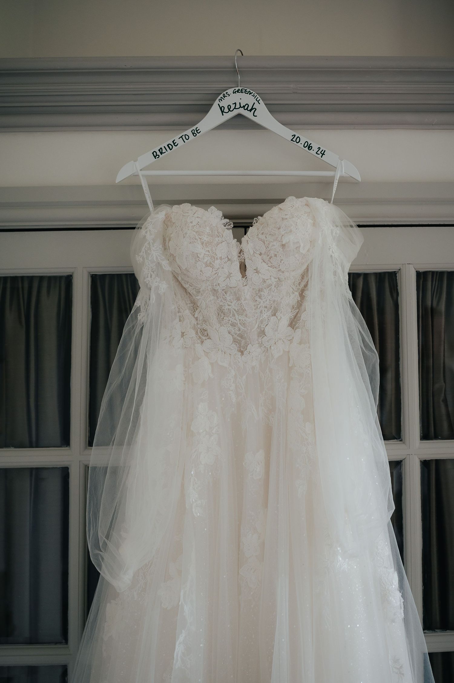 Delicate white wedding gown with lace bodice displayed on custom hanger.