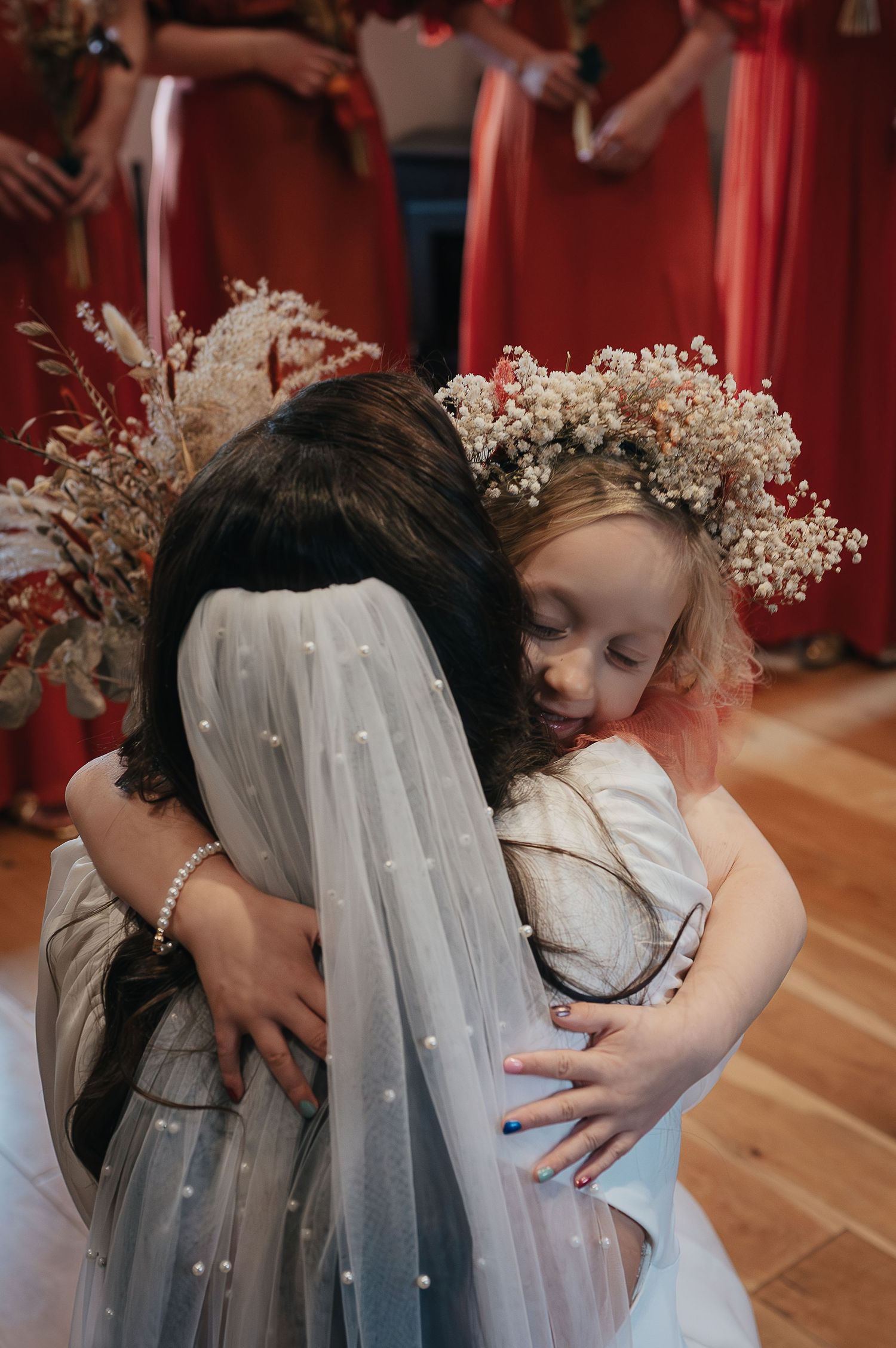 A sweet moment captured as a flower girl in coral hugs the bride wearing dried flower crowns.