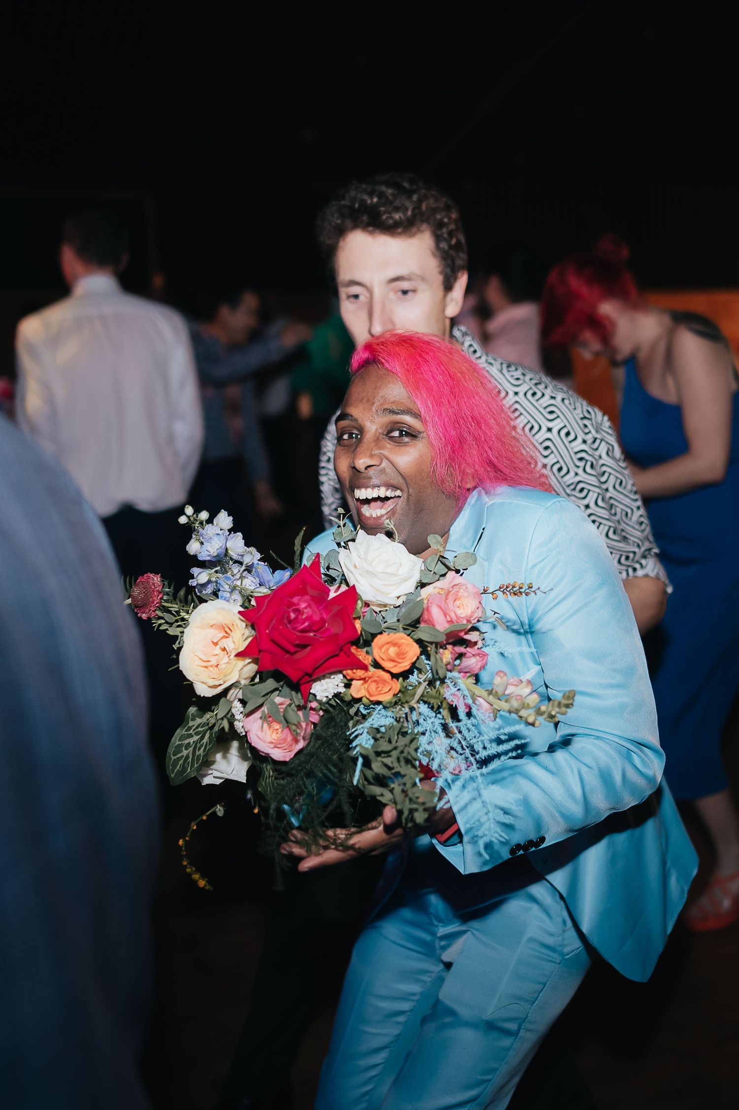 Person in bright blue outfit holding vibrant floral bouquet at celebration event.