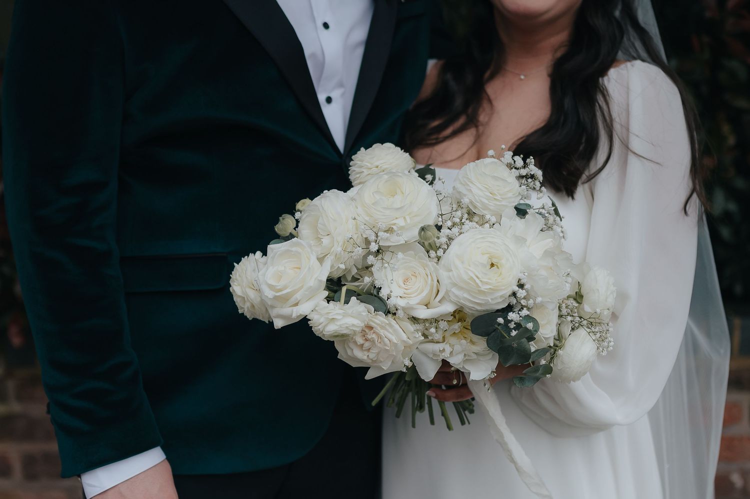Close-up of couple holding elegant white rose wedding bouquet.