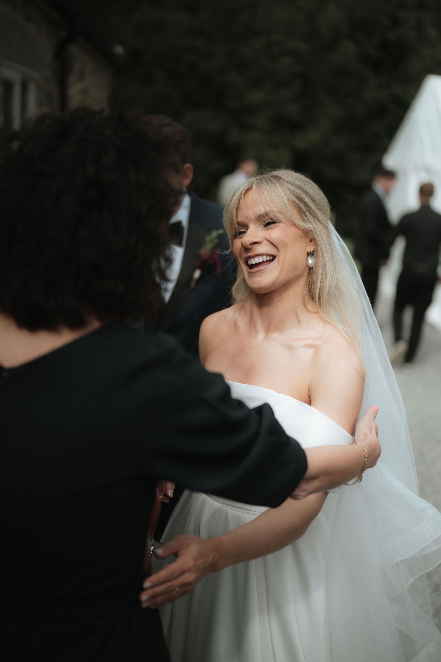 A bride in a strapless white wedding dress laughs joyfully while greeting guests at her wedding celebration.Blackton Grange Wedding. Luke Ha