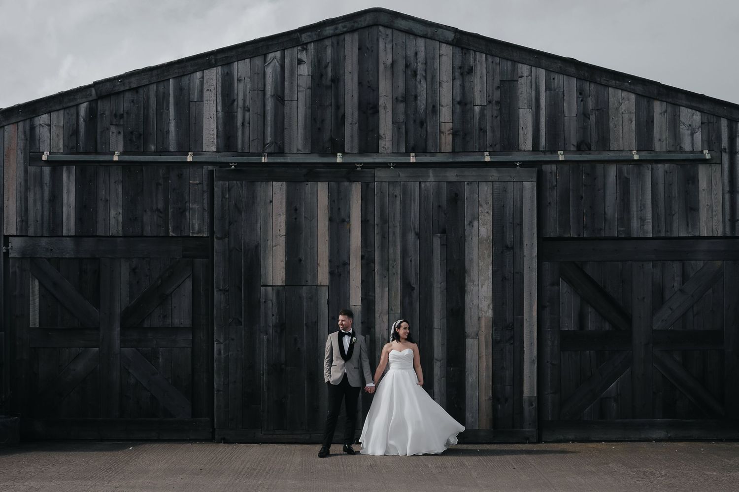 Wedding couple poses in front of a dramatic dark wooden barn exterior.