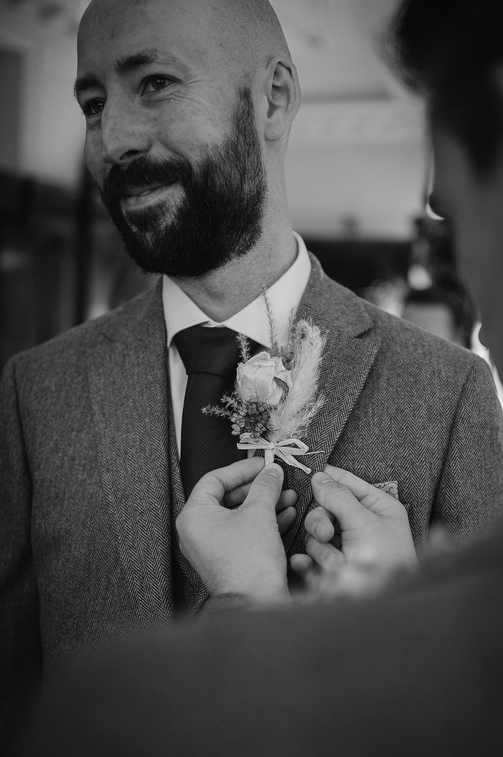 Boutonniere being pinned to lapel of grey suit in black and white.