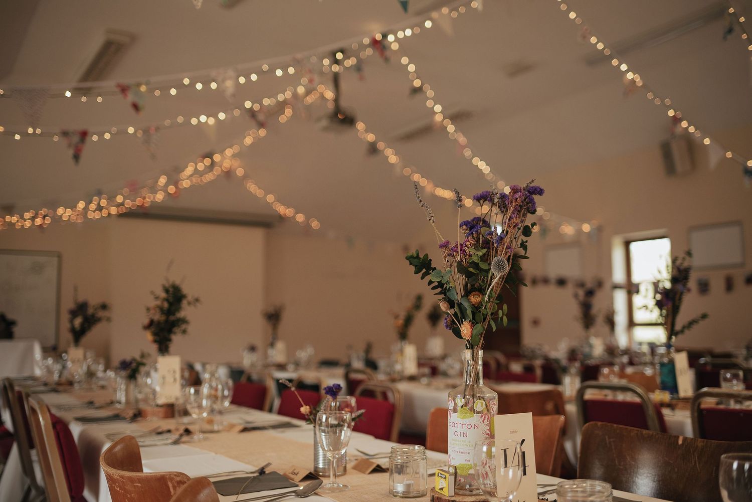 Wedding reception tables set with flowers and glowing string lights create an intimate atmosphere.