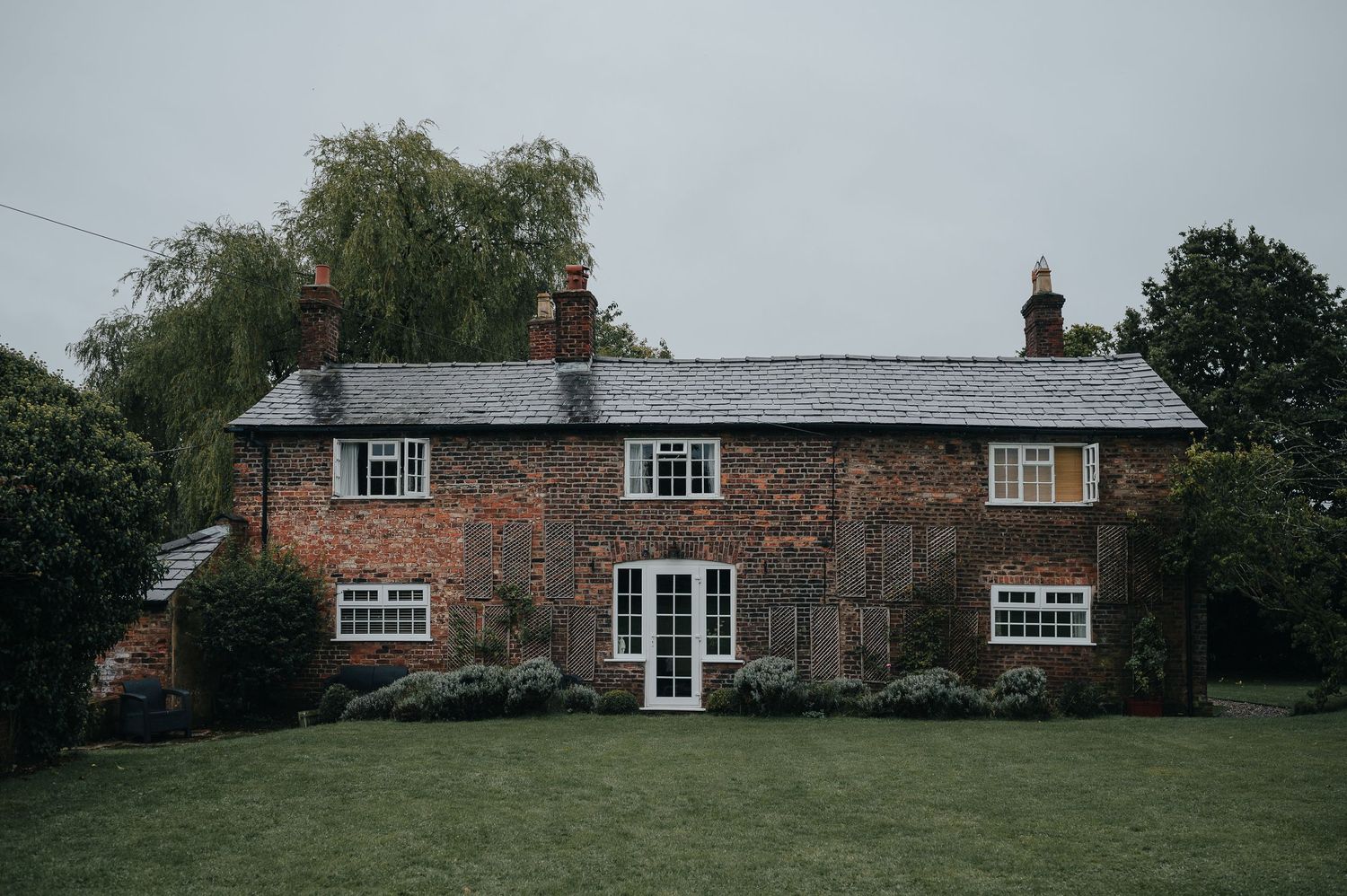 Traditional brick cottage with slate roof and French doors set in green garden.