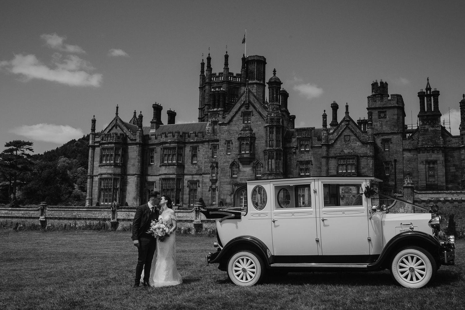 Classic vintage car parked in front of a Gothic castle during a wedding photoshoot.